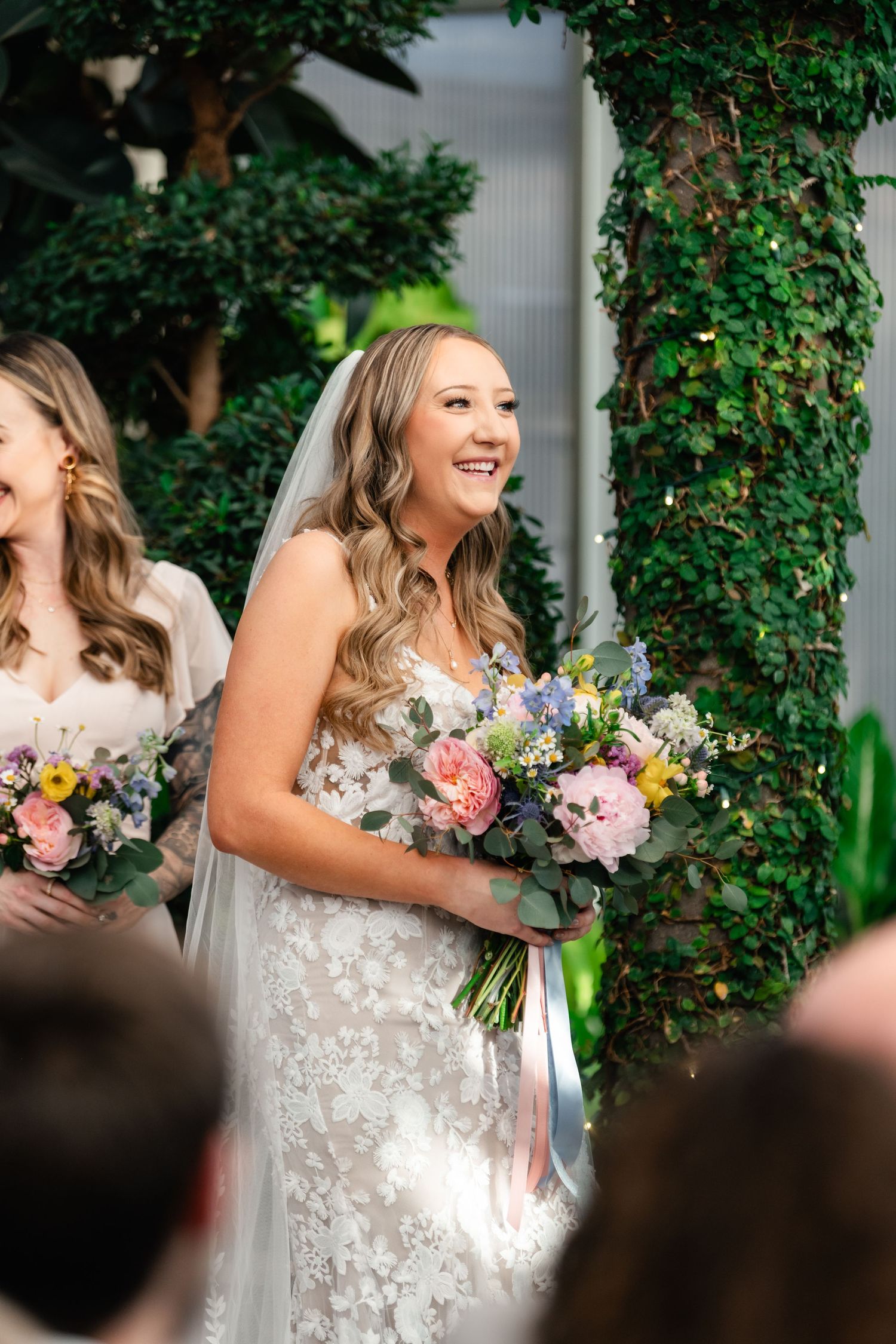 A joyful scene at a wedding with white pillars and lush greenery, featuring a beautiful bouquet of mixed flowers.
