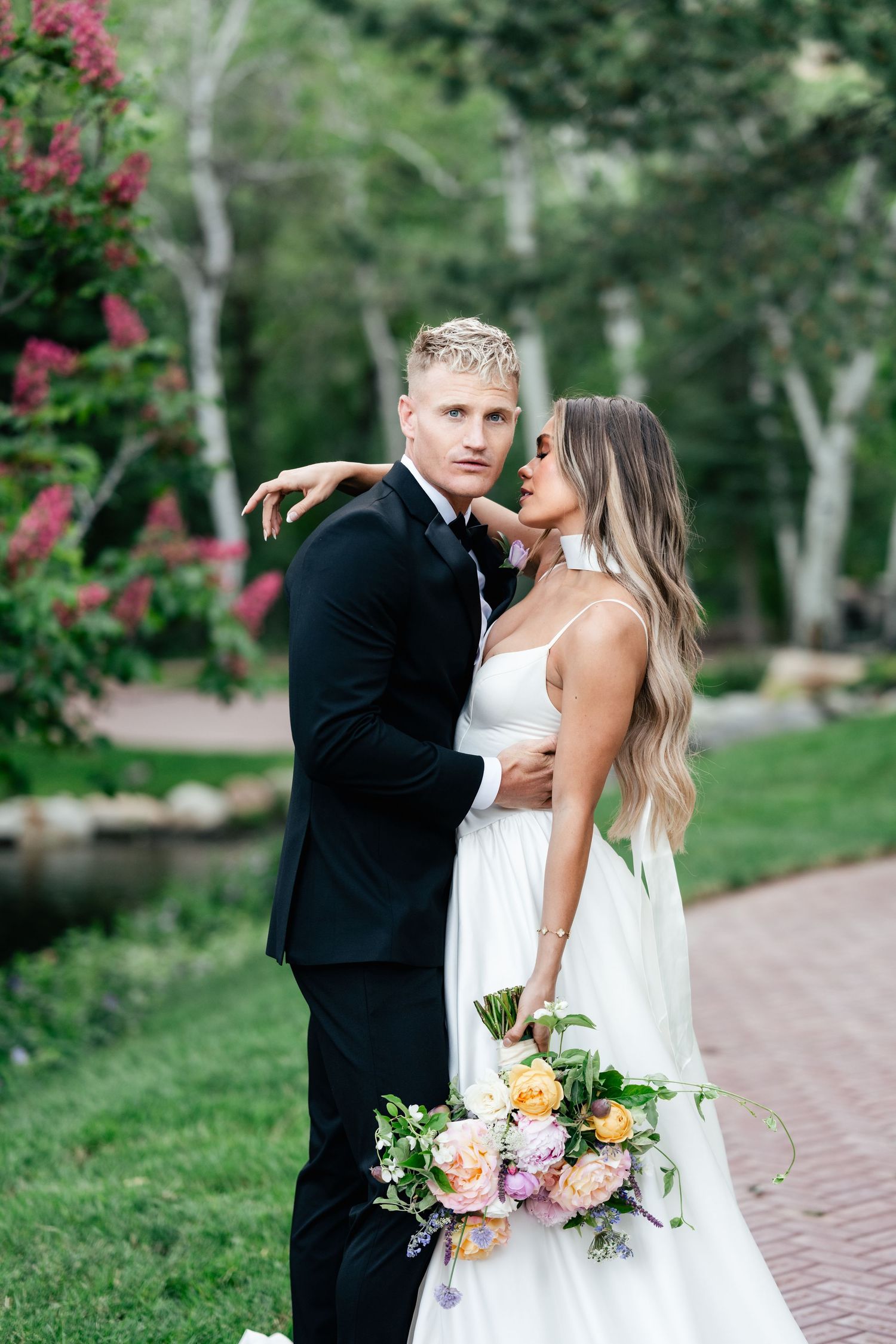 A romantic moment captured in a garden setting with beautiful floral bouquet and elegant wedding attire.