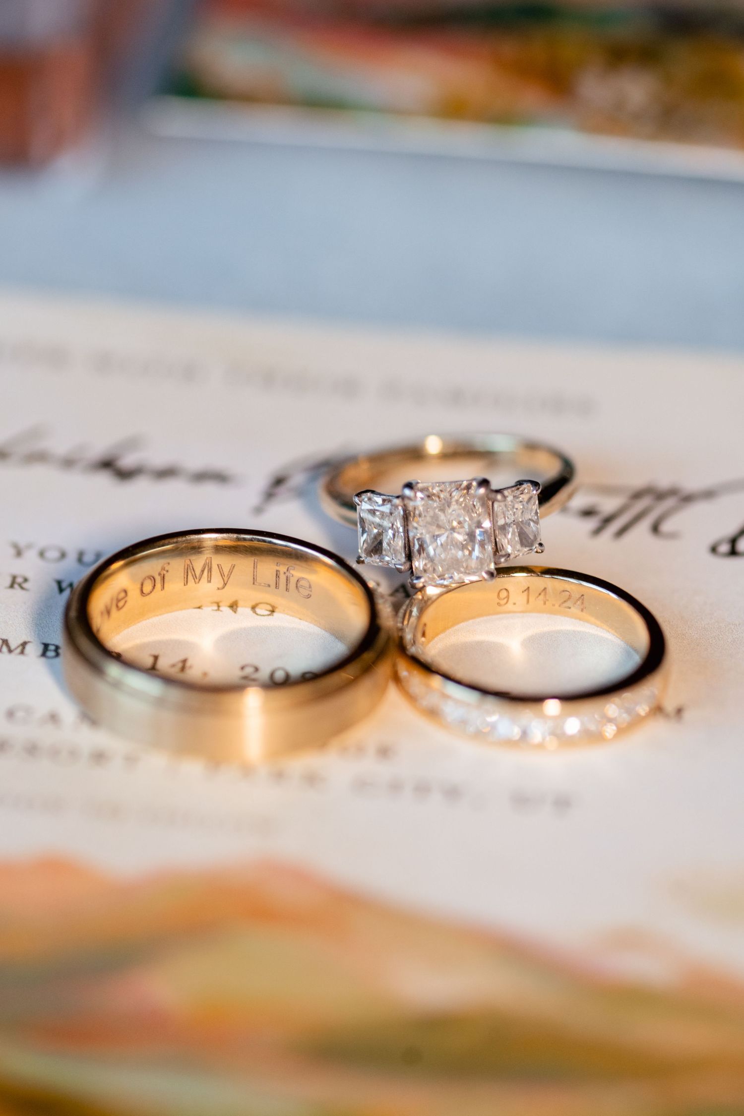 Three wedding rings including a diamond engagement ring displayed on paper with elegant script text. Park City Wedding Photographer.