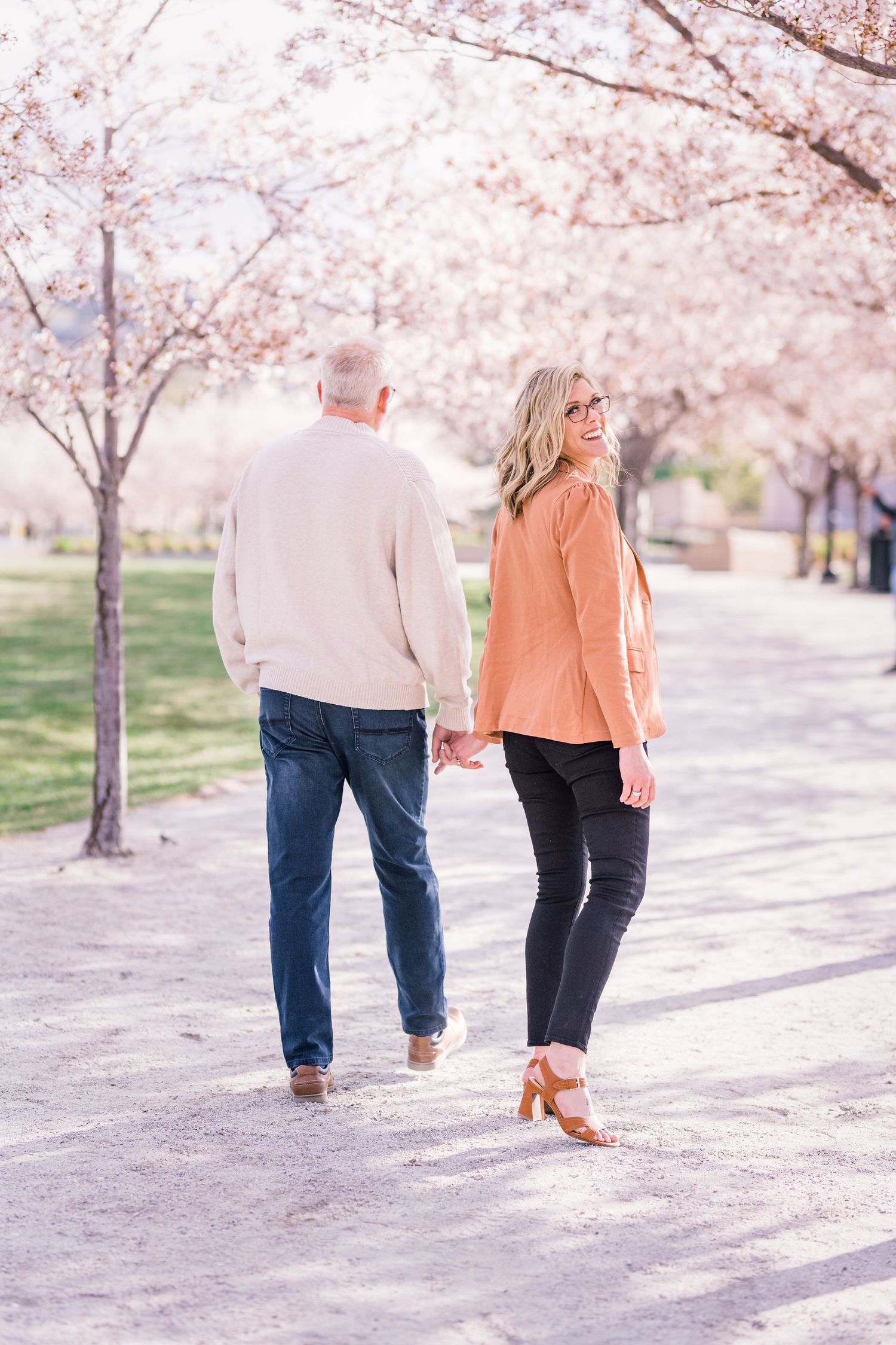 A couple strolls beneath blooming cherry blossoms on a spring day.