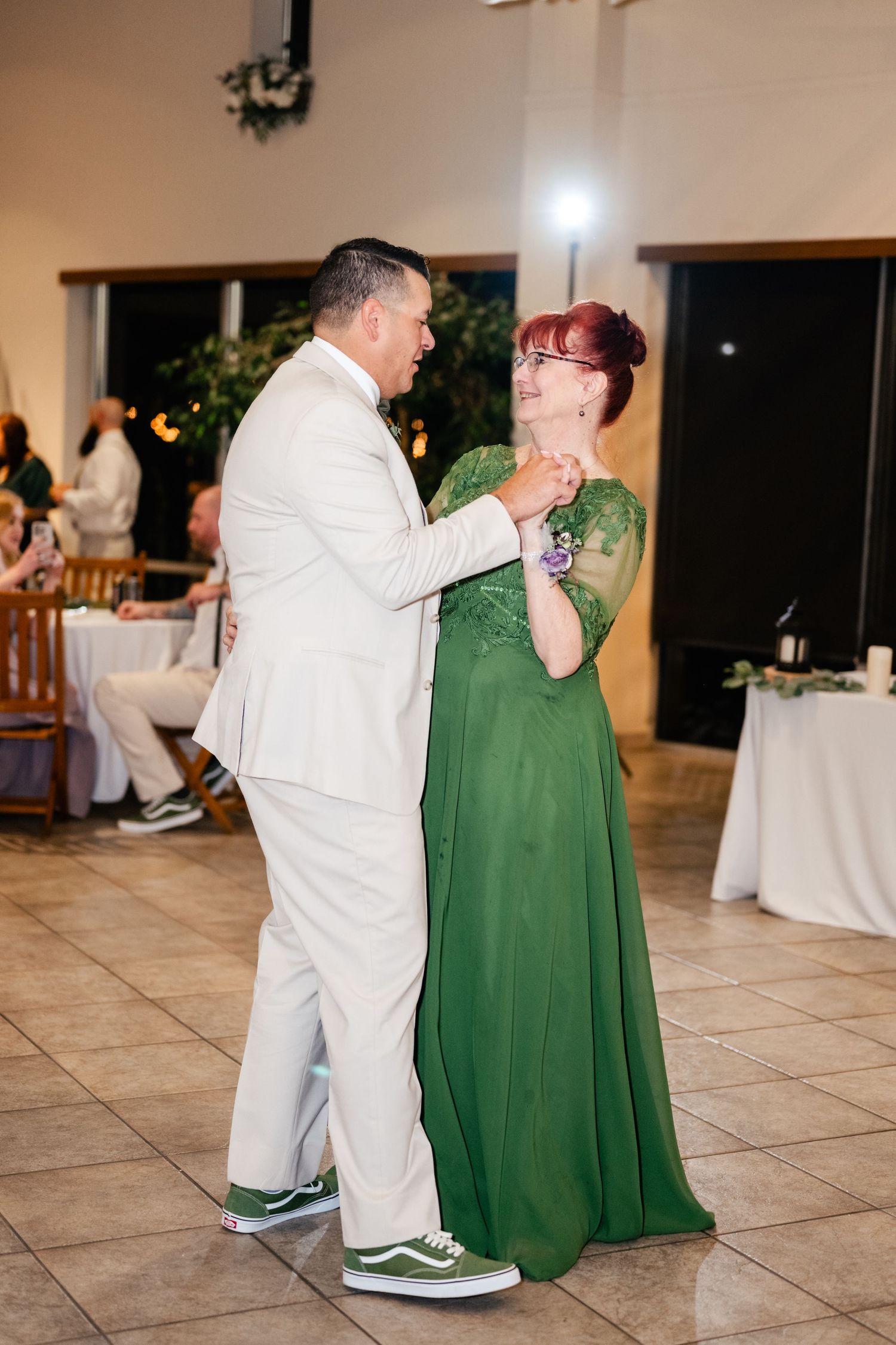 A couple dances together at a wedding reception, with the woman wearing an elegant emerald green gown and the man in white.