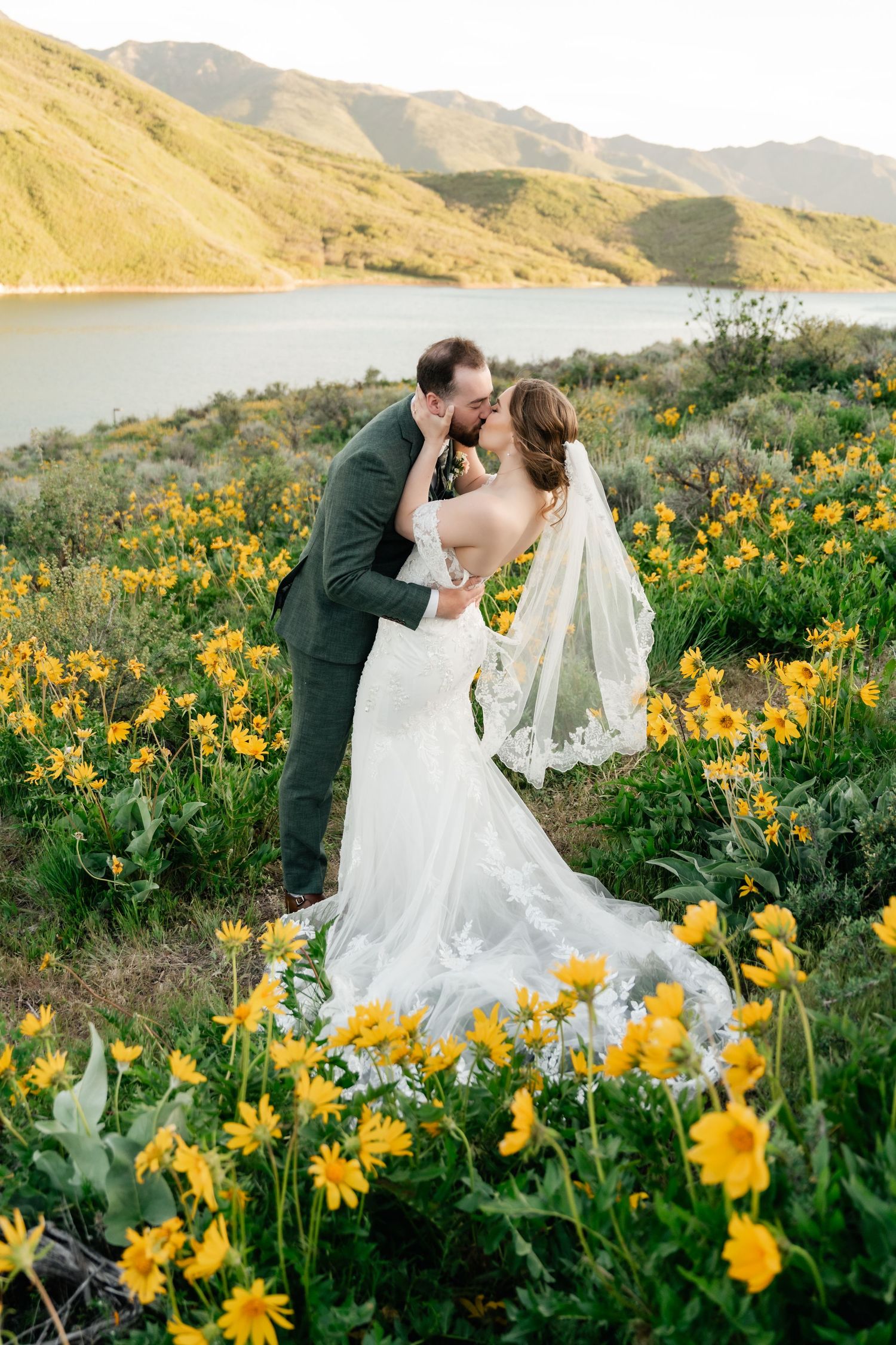Wedding couple shares romantic moment in field of yellow wildflowers with mountain backdrop. Mountain Wedding Photographer.