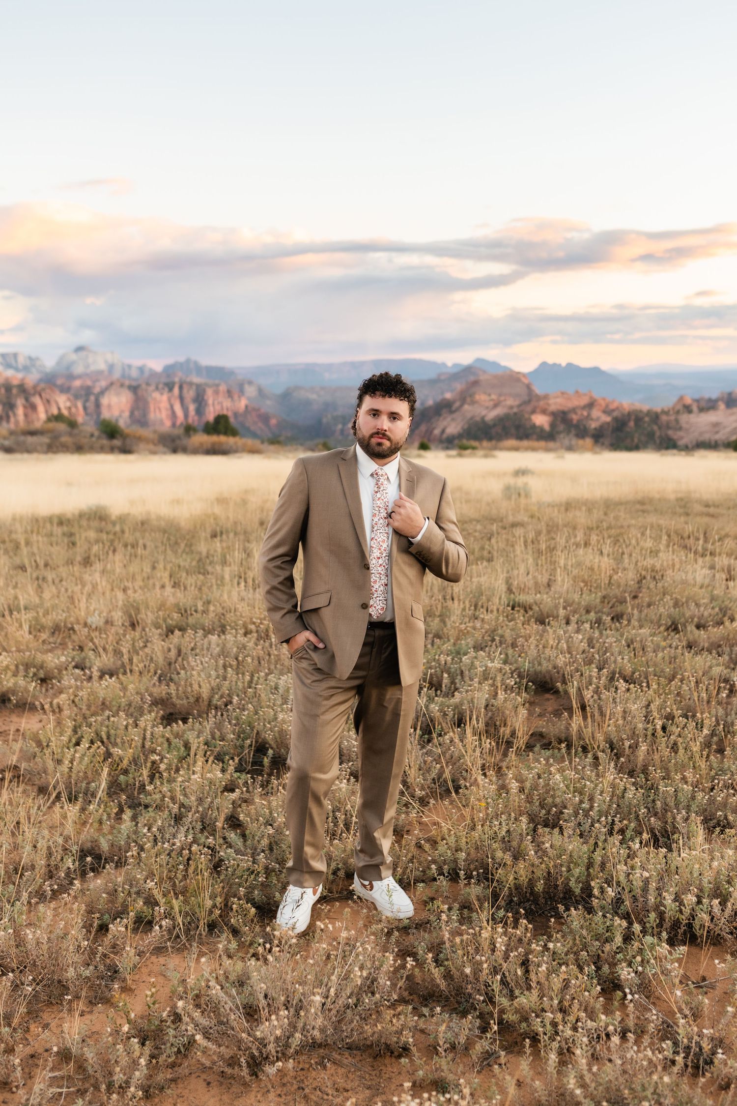 A person in a tan suit strikes playful poses in a desert landscape at sunset.