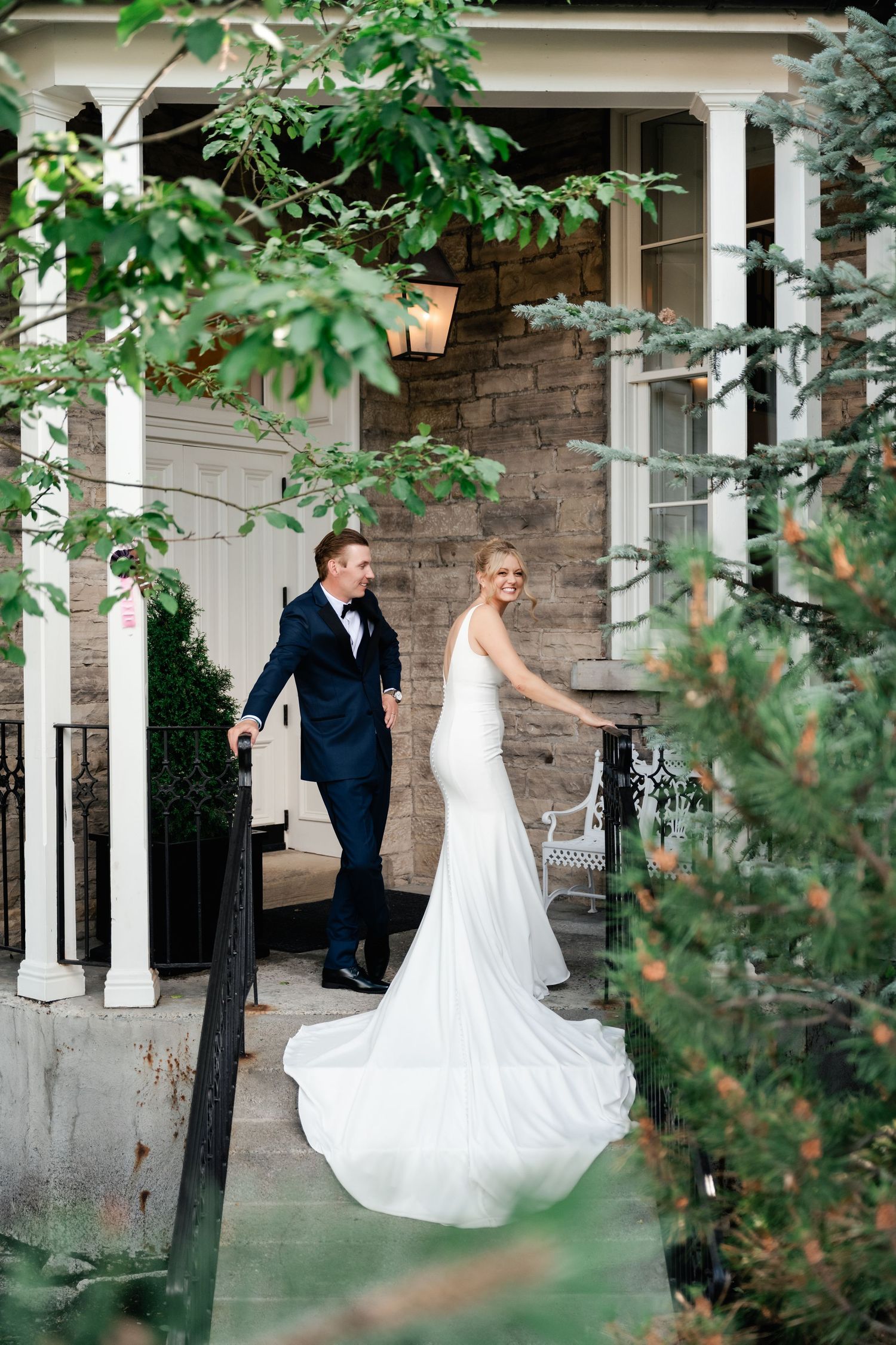 Wedding couple shares a tender moment on a classic stone veranda with white pillars.
