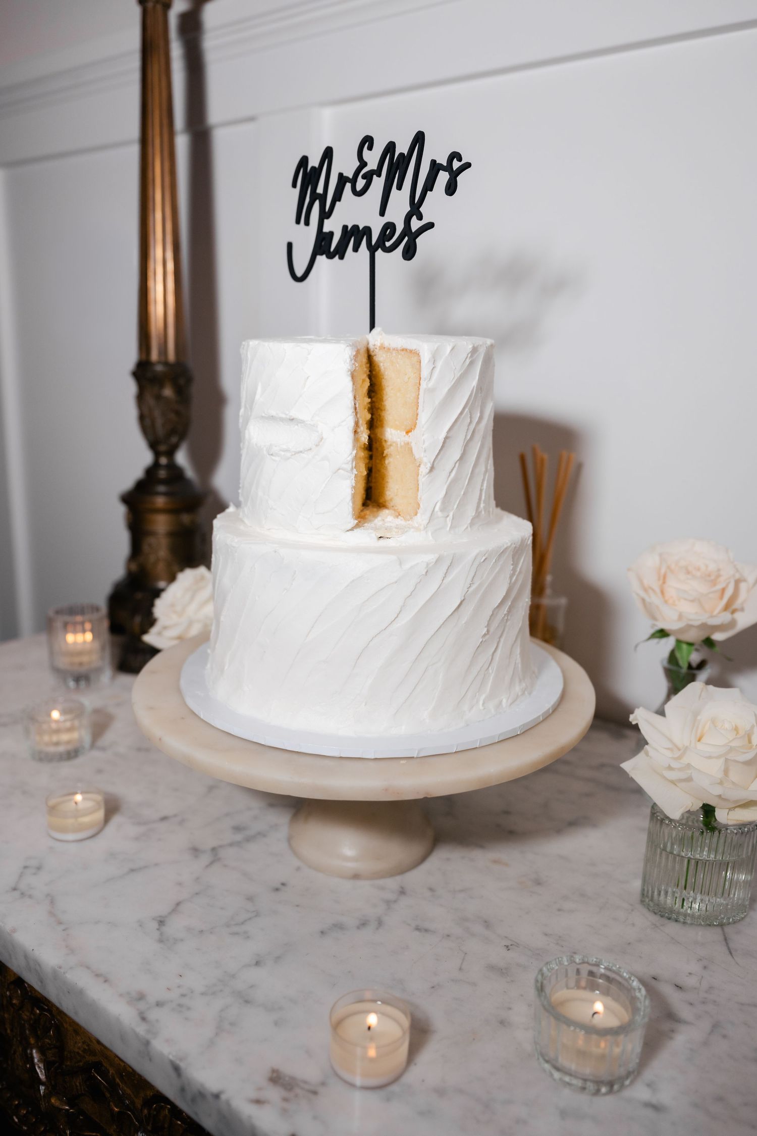 White wedding cake with elegant textured frosting displayed on marble table with glowing candles.