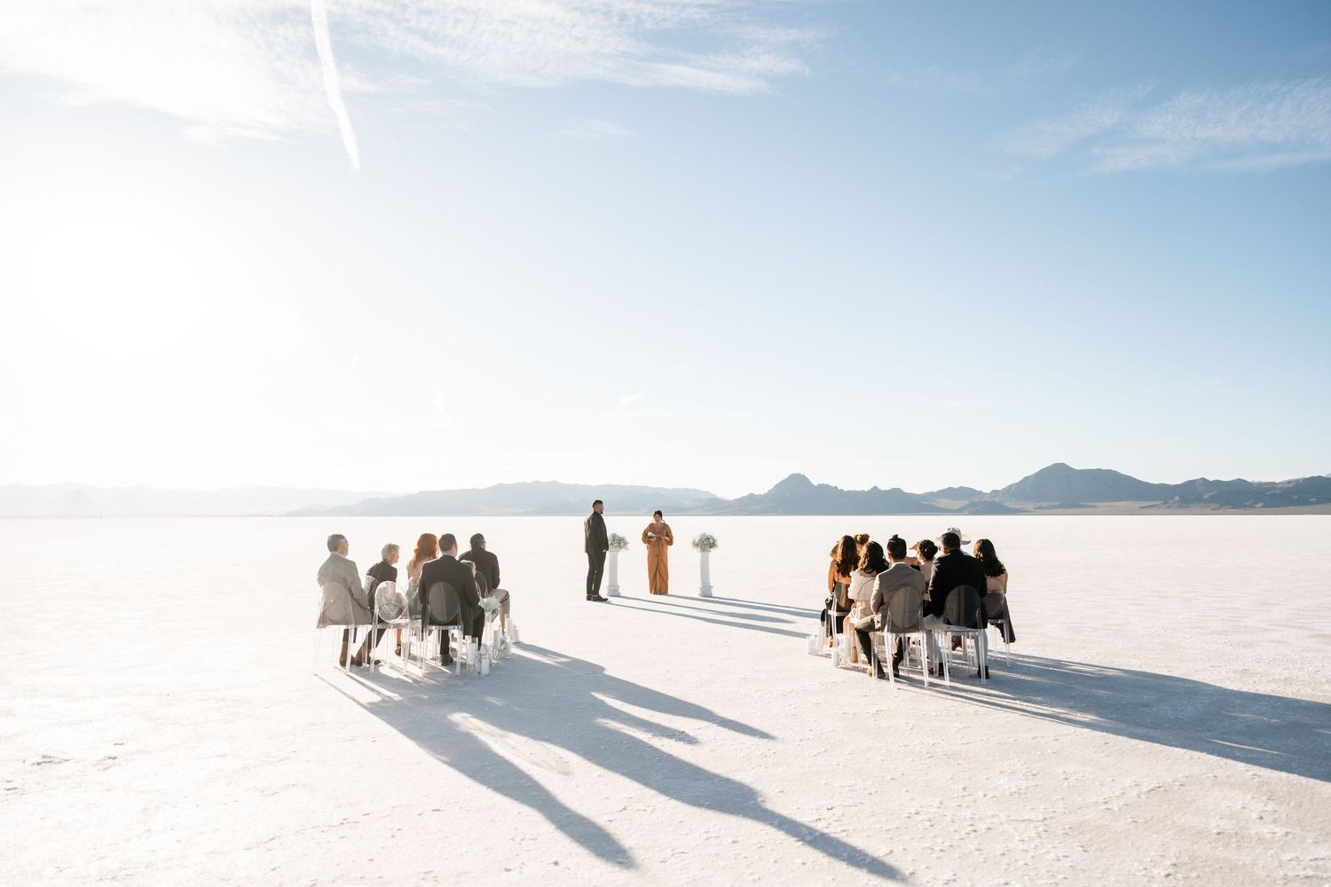 A group walks together across the vast white expanse of Bonneville Salt Flats under bright blue skies.