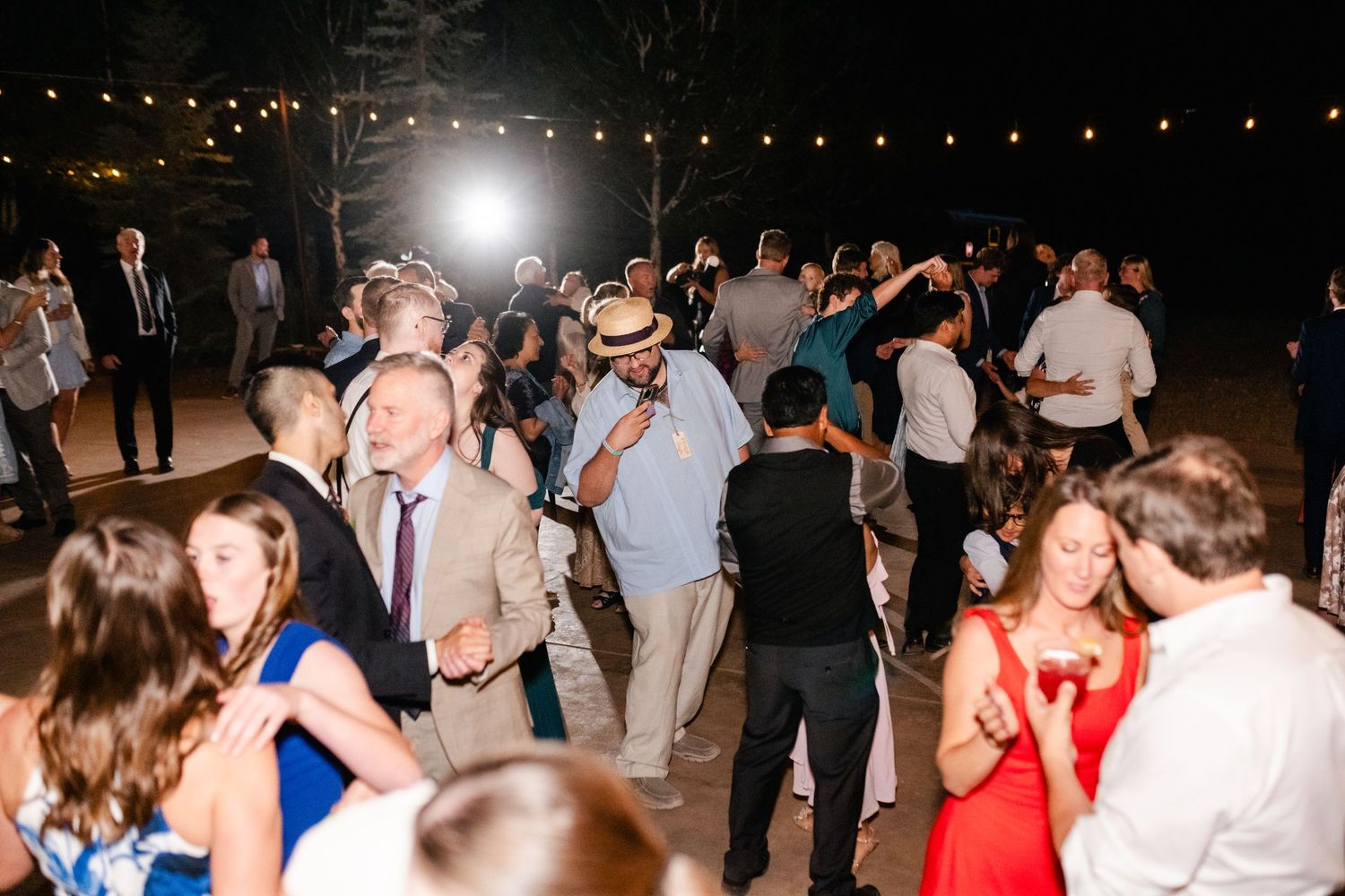 Guests dance under string lights at nighttime wedding reception.