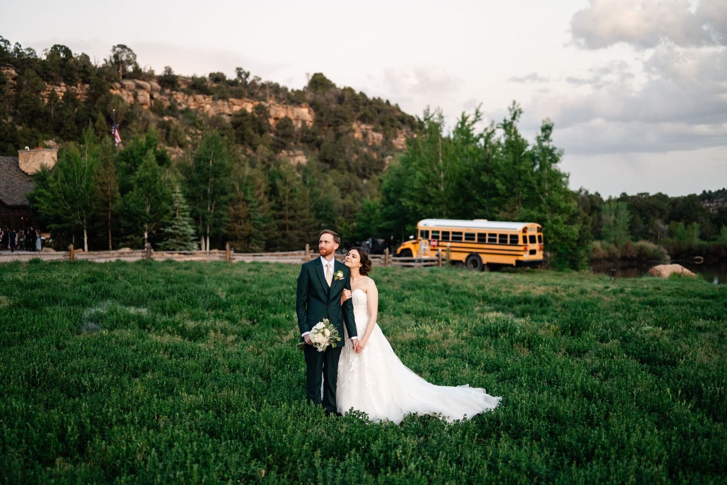 Scenic mountain wedding photos with yellow school bus parked in background and couple posing in grassy meadow.