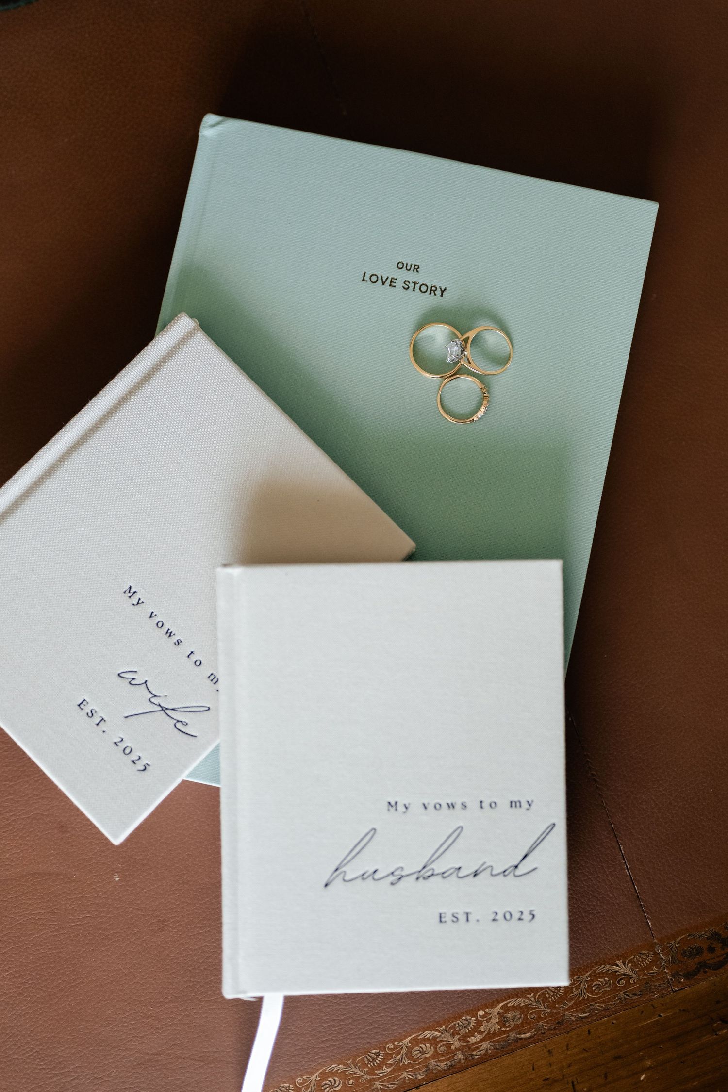 Wedding vow books and gold rings arranged on a wooden surface with mint green accents.