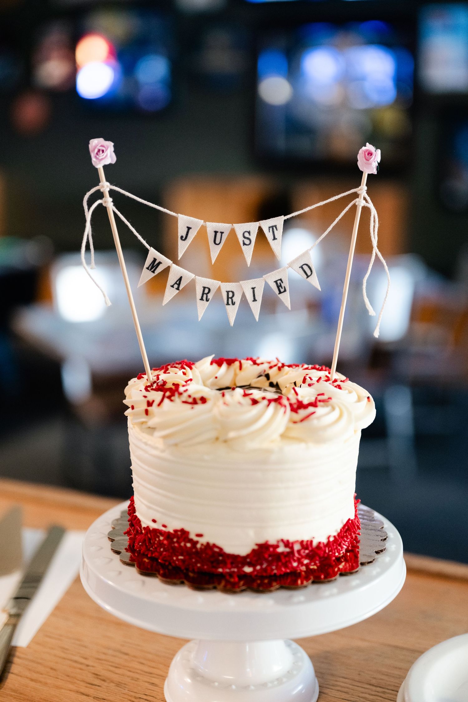 Red velvet wedding cake with white frosting and small bunting banner on white cake stand.