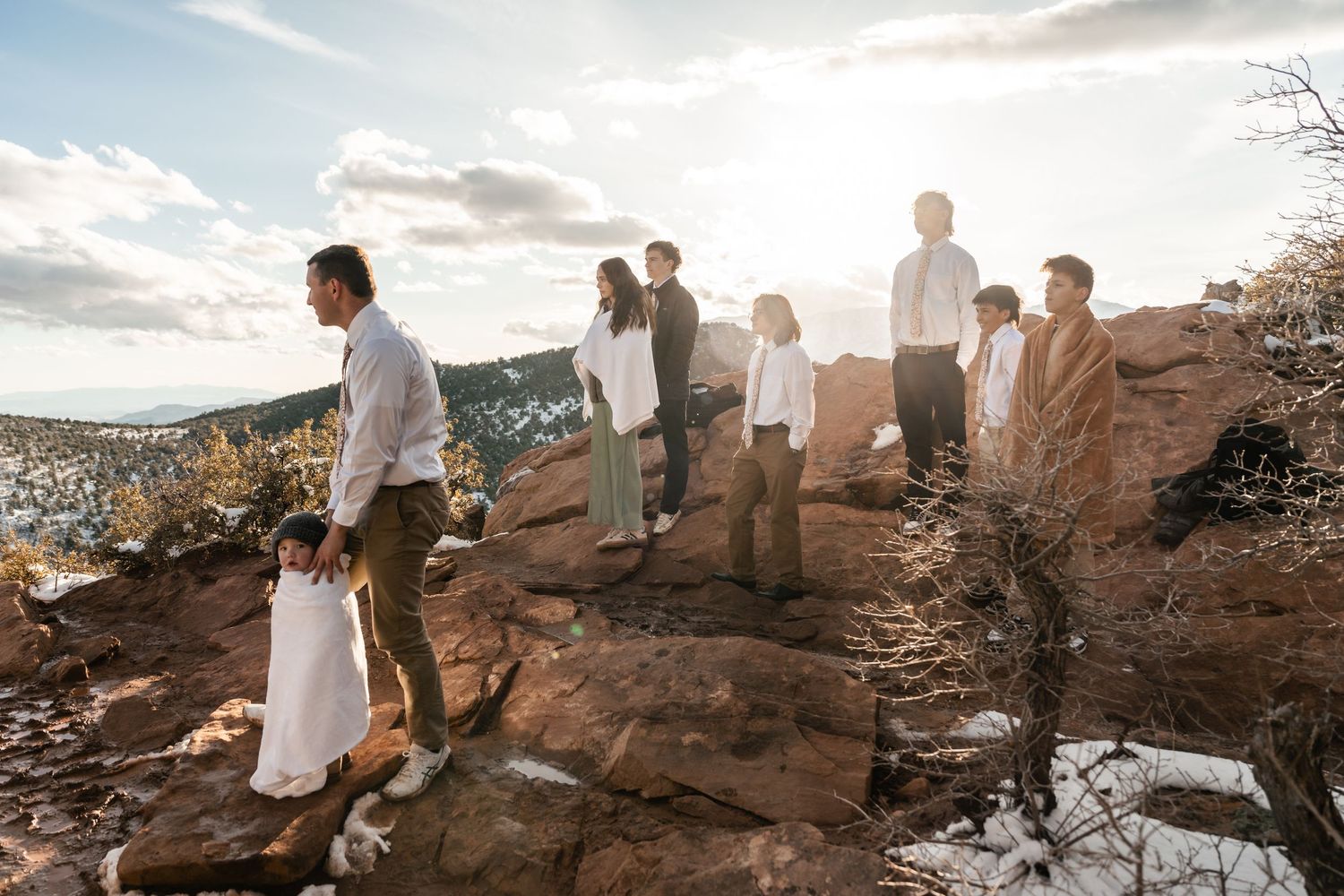 People walking along snow-covered red rock formations at sunset.