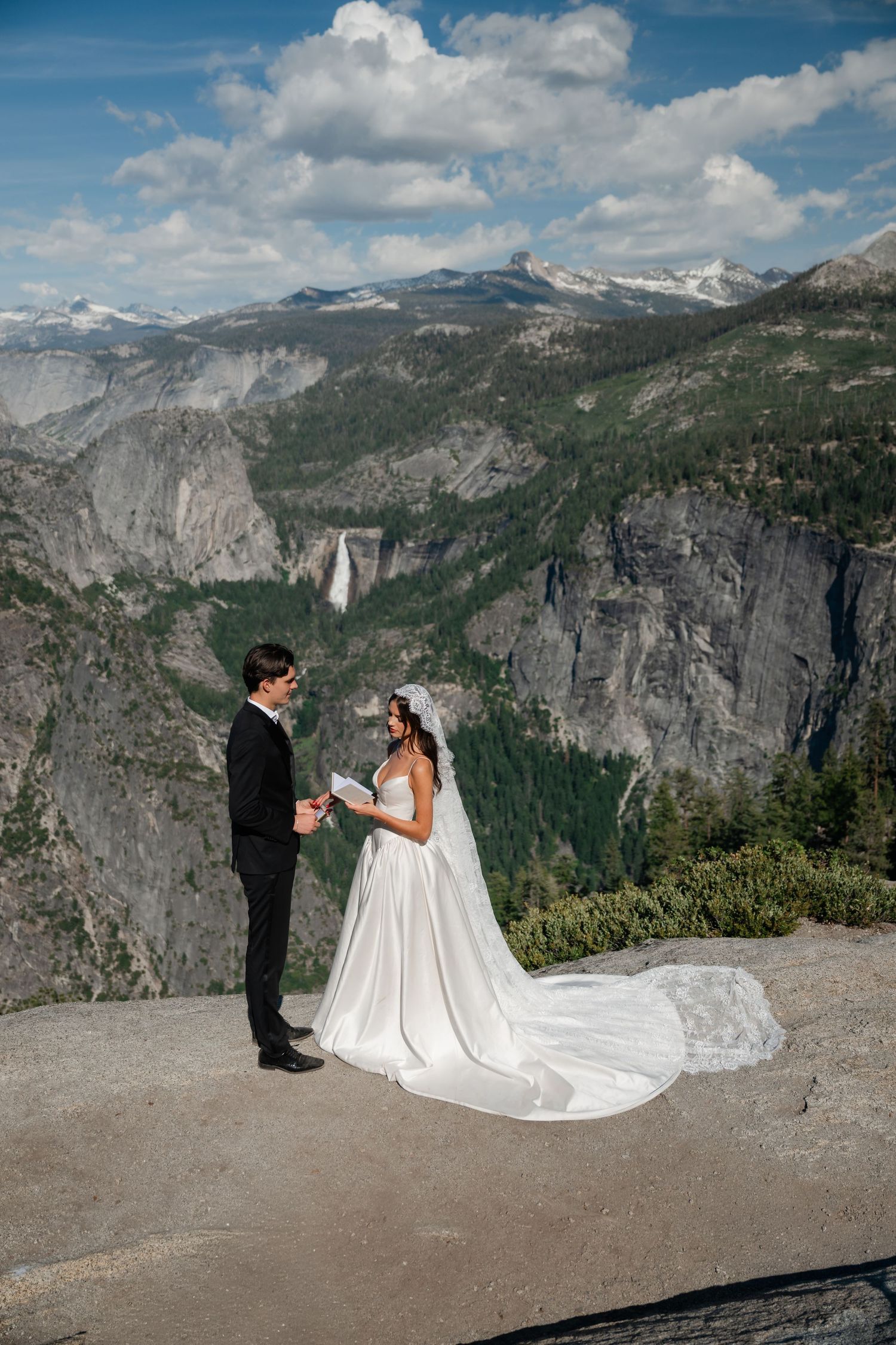 Bride and groom exchange vows on a scenic Yosemite overlook with waterfall and mountain views.