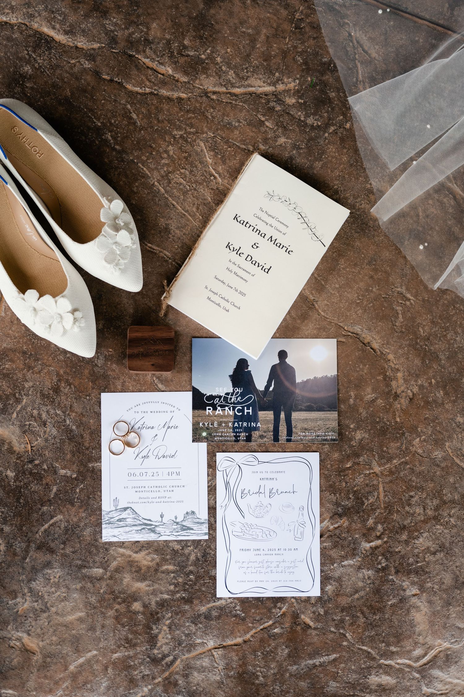 Wedding invitations and white bridal shoes arranged on a textured stone surface.