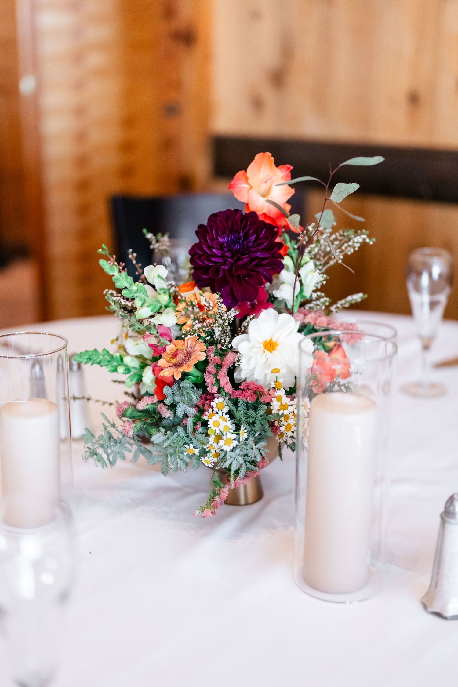 Vibrant floral centerpiece with burgundy dahlia, coral roses, and white flowers on a wedding reception table.