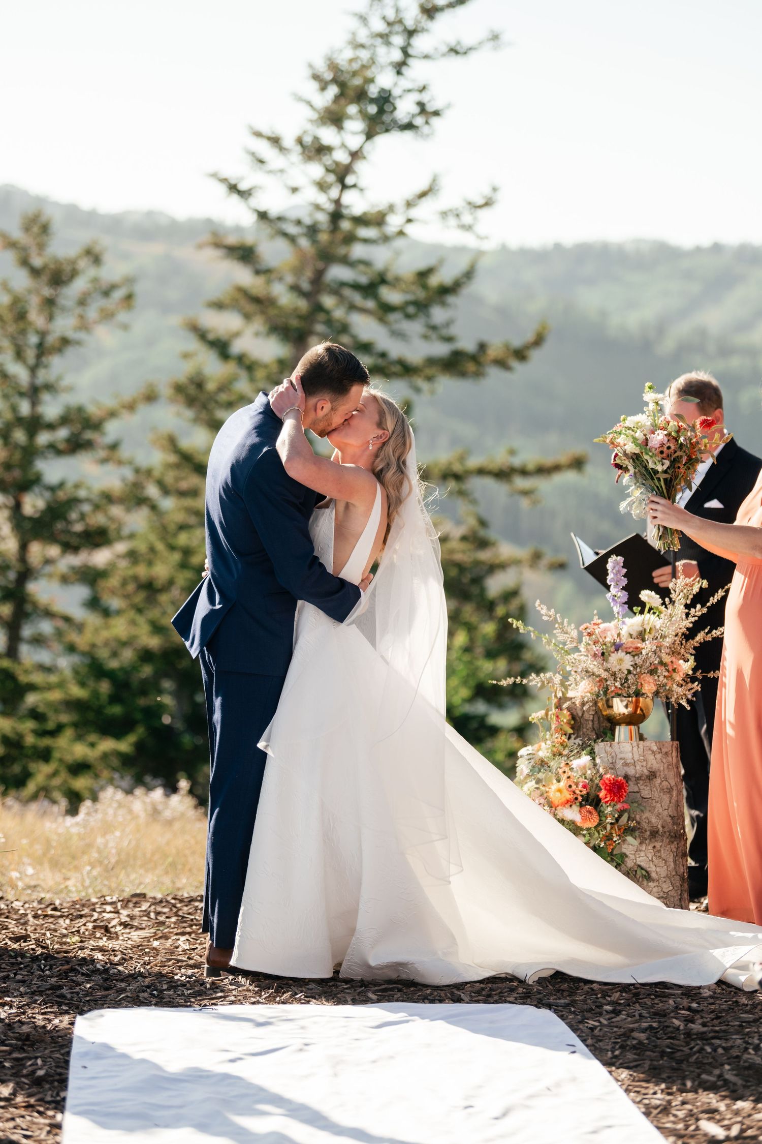 Romantic wedding ceremony moment captured against scenic mountain landscape with evergreen trees.