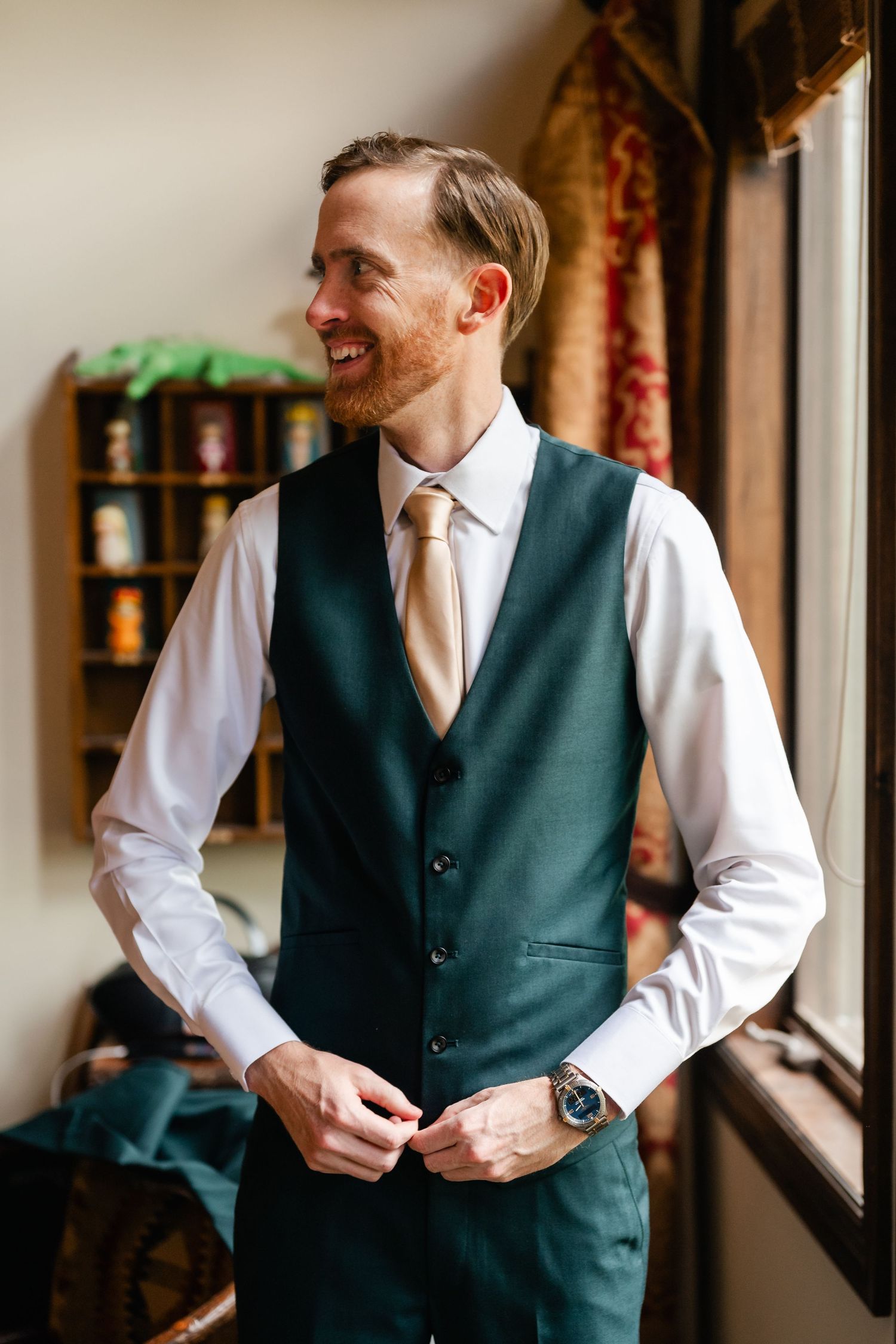 Person in formal attire with green vest and white shirt adjusting clothing near window.