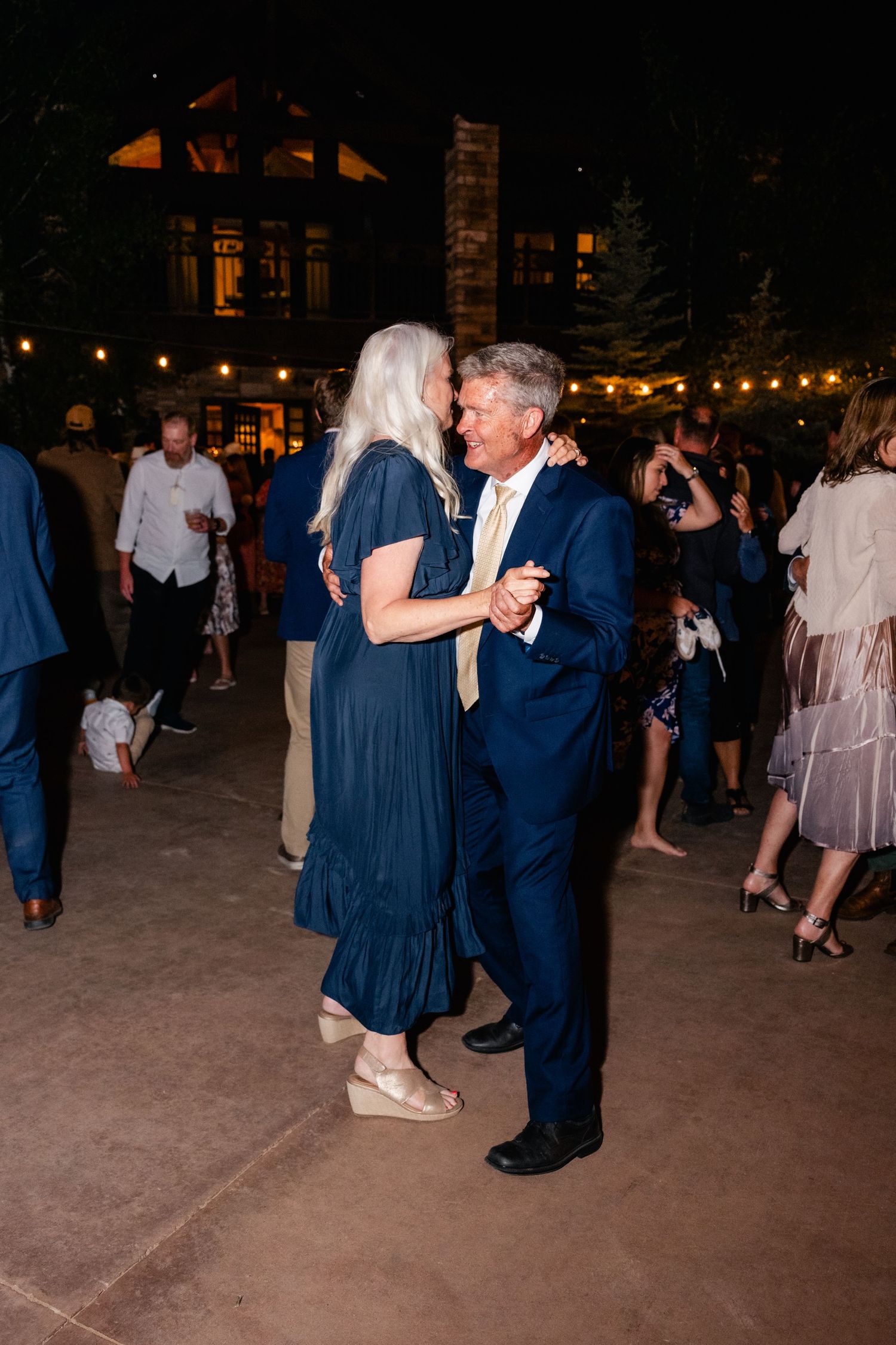 Couples dance together under twinkling lights at an evening wedding reception.