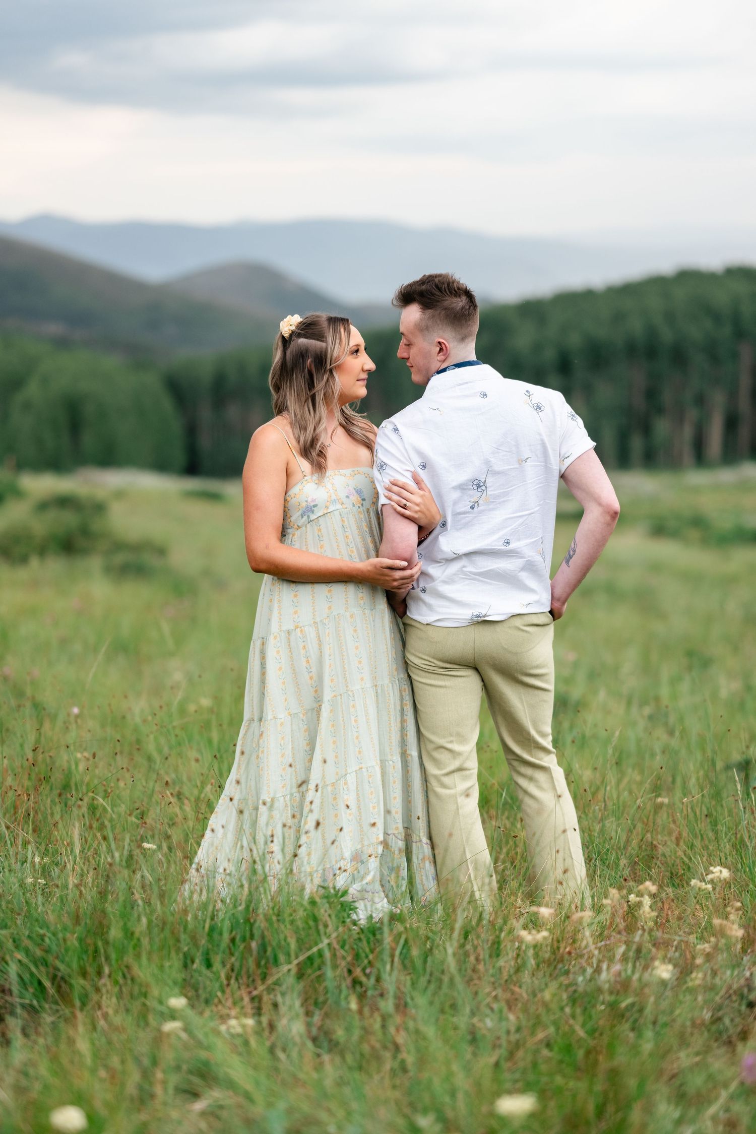 A couple shares a tender moment while standing in a mountain meadow filled with wildflowers.