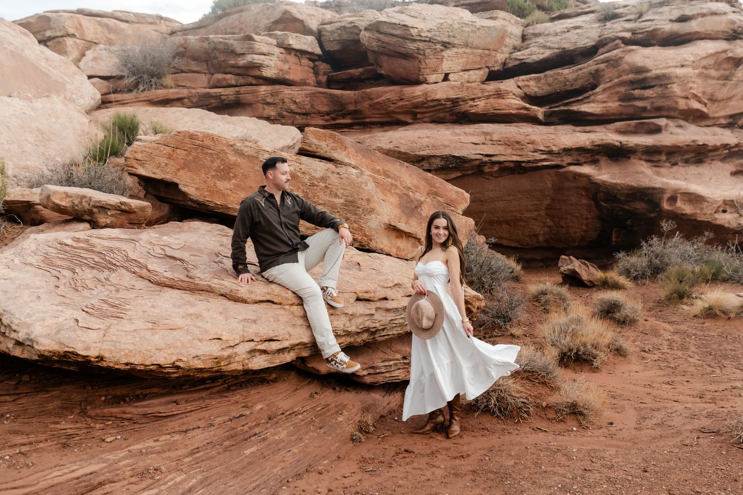 Playful couple posing on red rock formations in desert landscape.