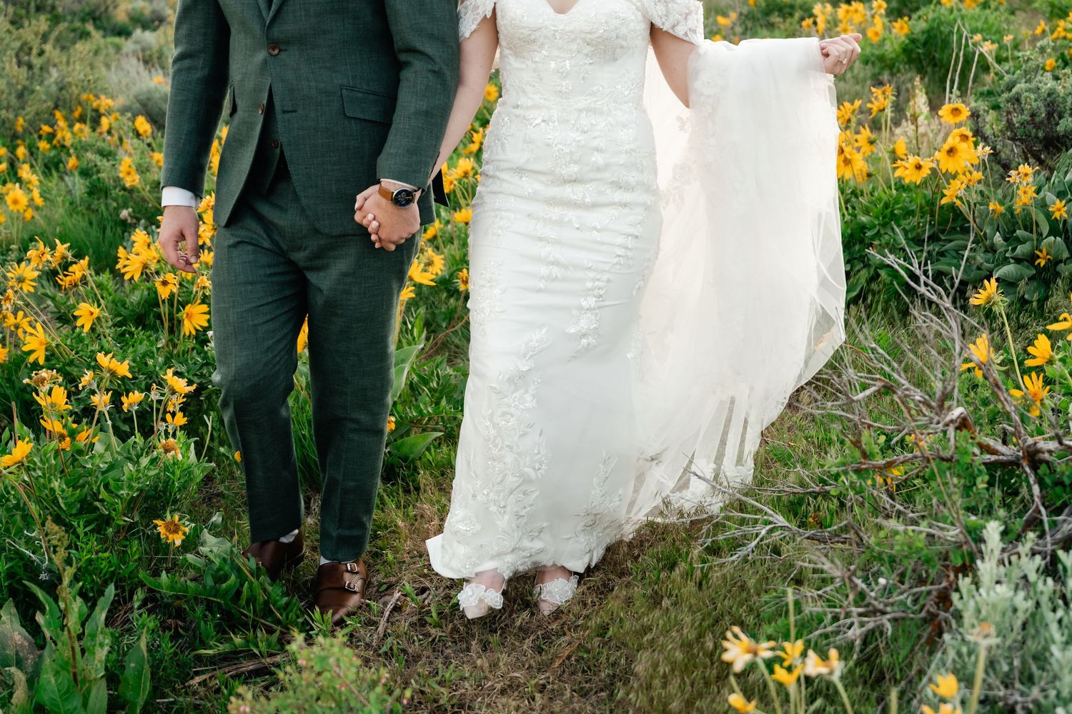 Wedding couple walking through a meadow filled with golden wildflowers and mountain views.