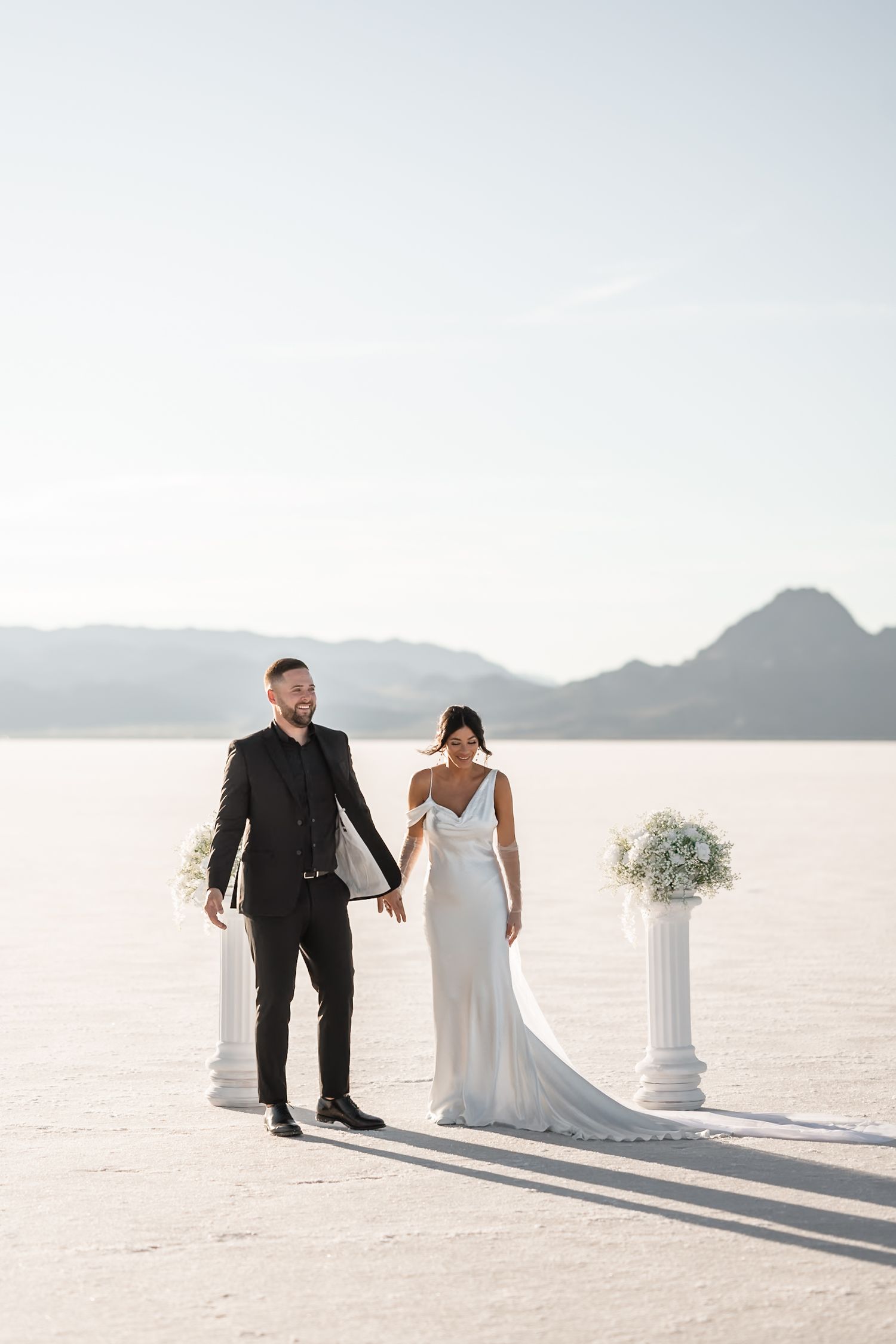 Wedding couple shares intimate moments on vast salt flats with decorative white columns.