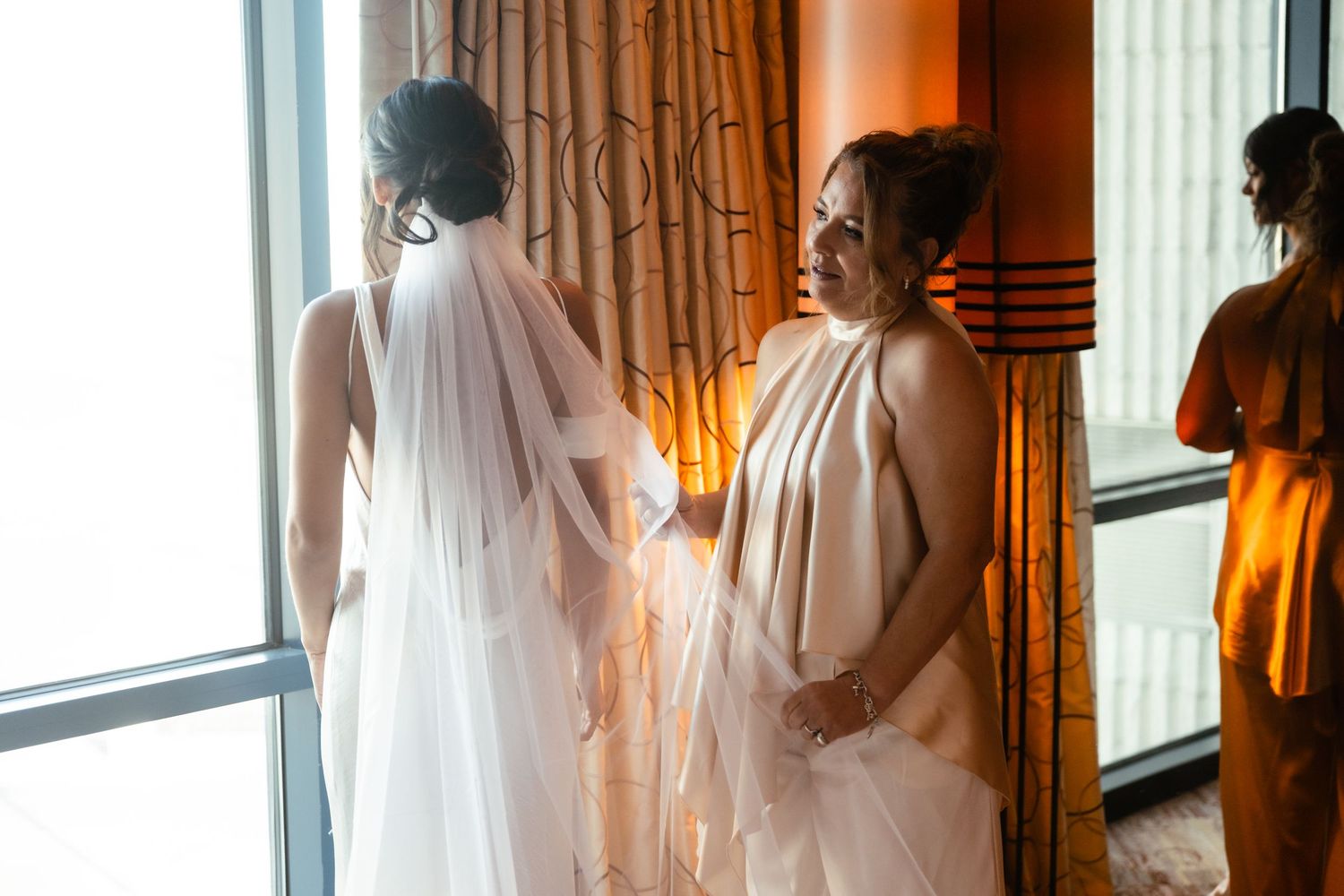 A series of silhouetted figures stand near windows in a warmly lit room with flowing curtains.
