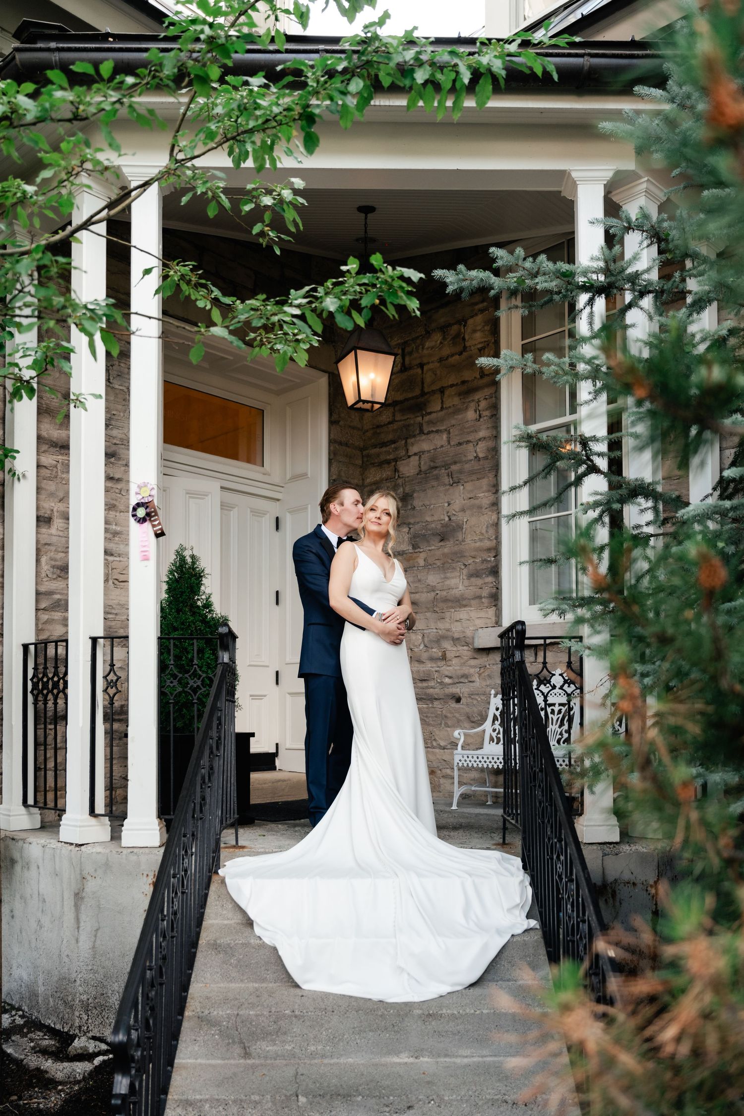 A romantic wedding portrait captured on a stone porch with elegant columns and iron railings.