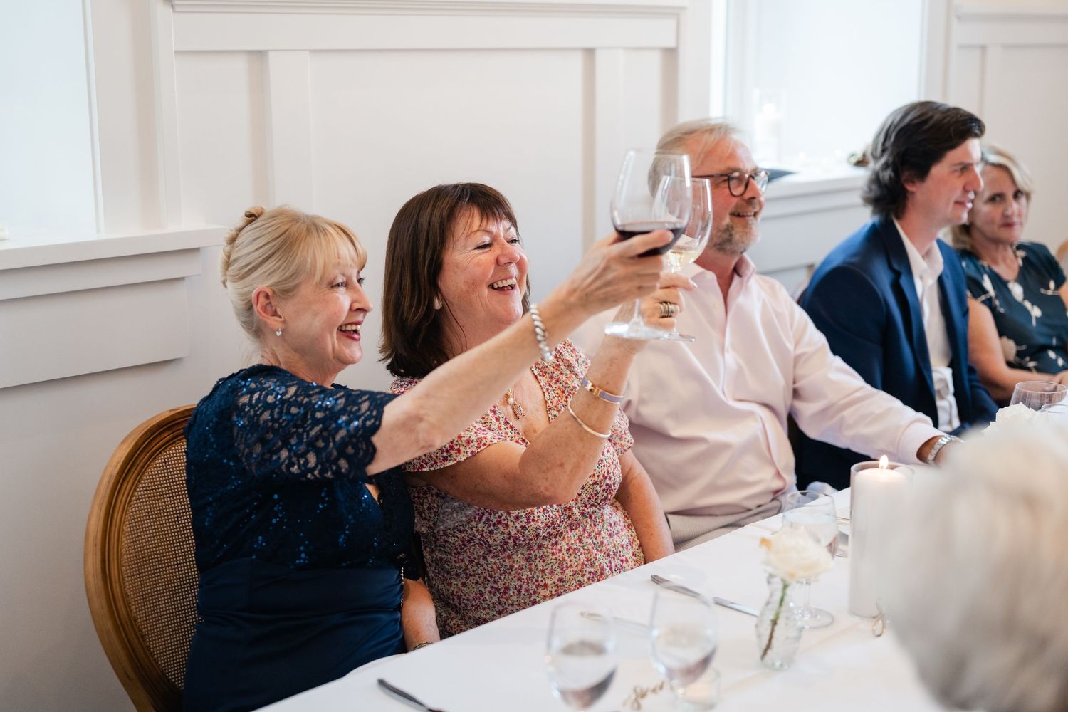 Wedding guests laugh and socialize at elegant white-clothed dining tables.