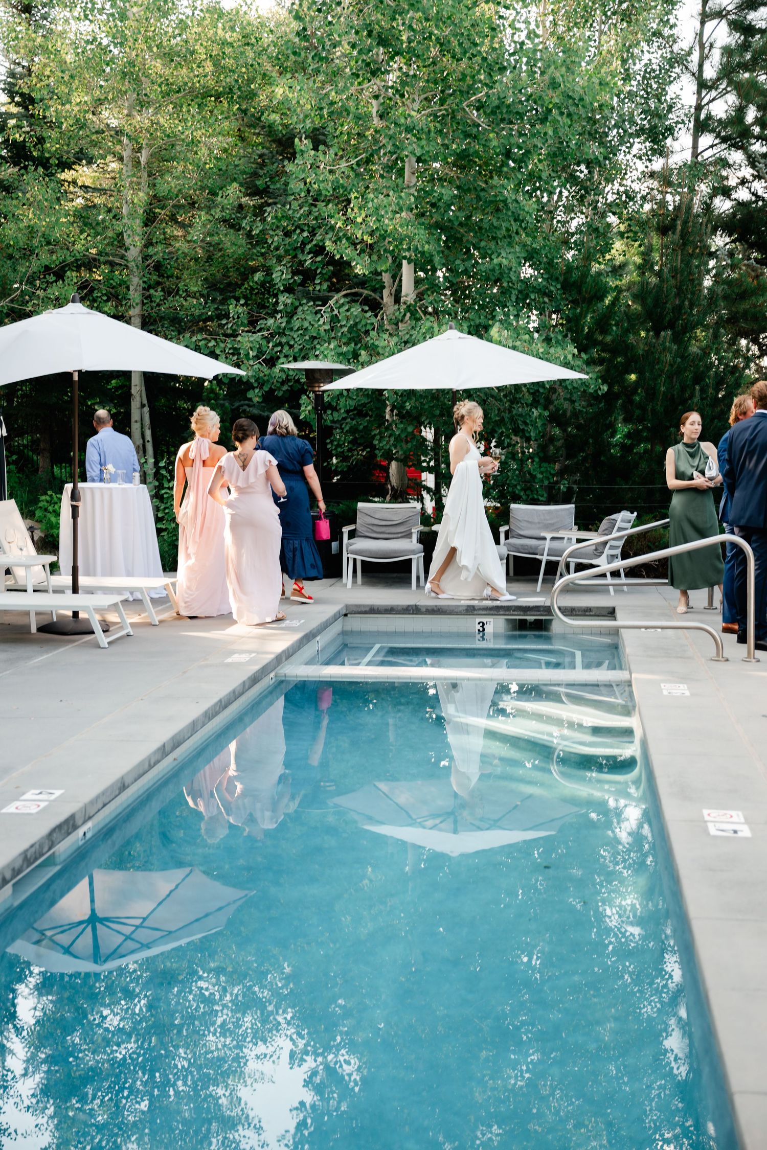 Elegant outdoor pool area with white patio furniture and guests enjoying a wedding celebration.