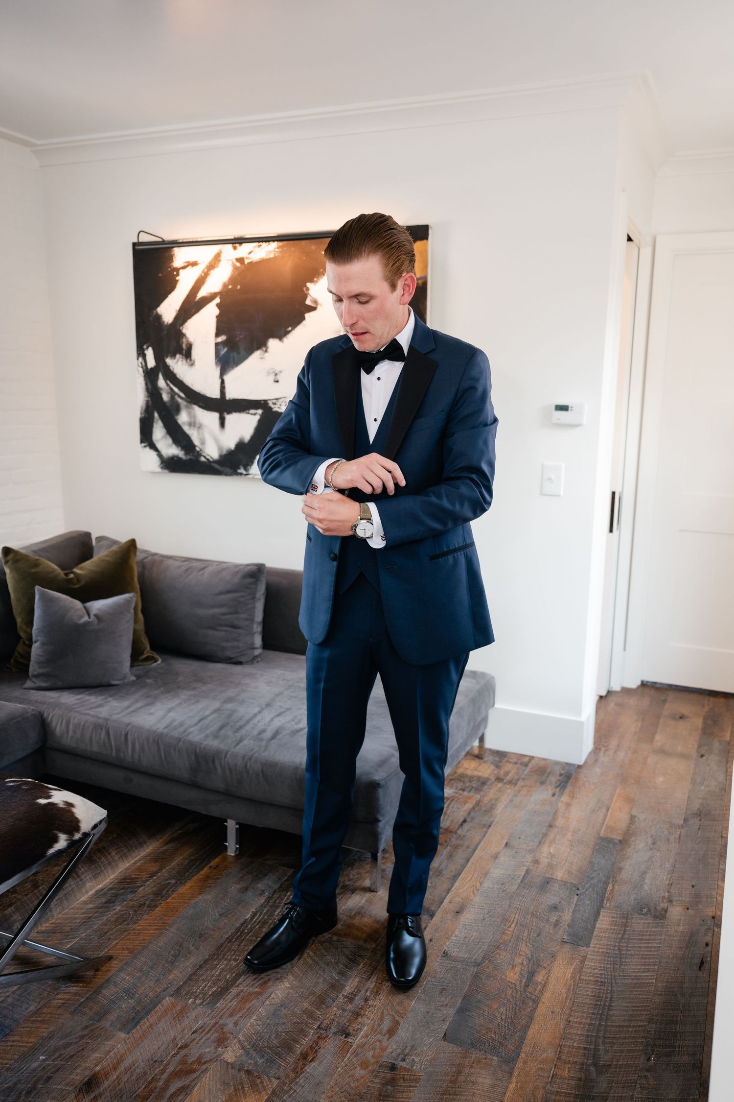 Person in navy tuxedo demonstrating dance moves on wooden floor.