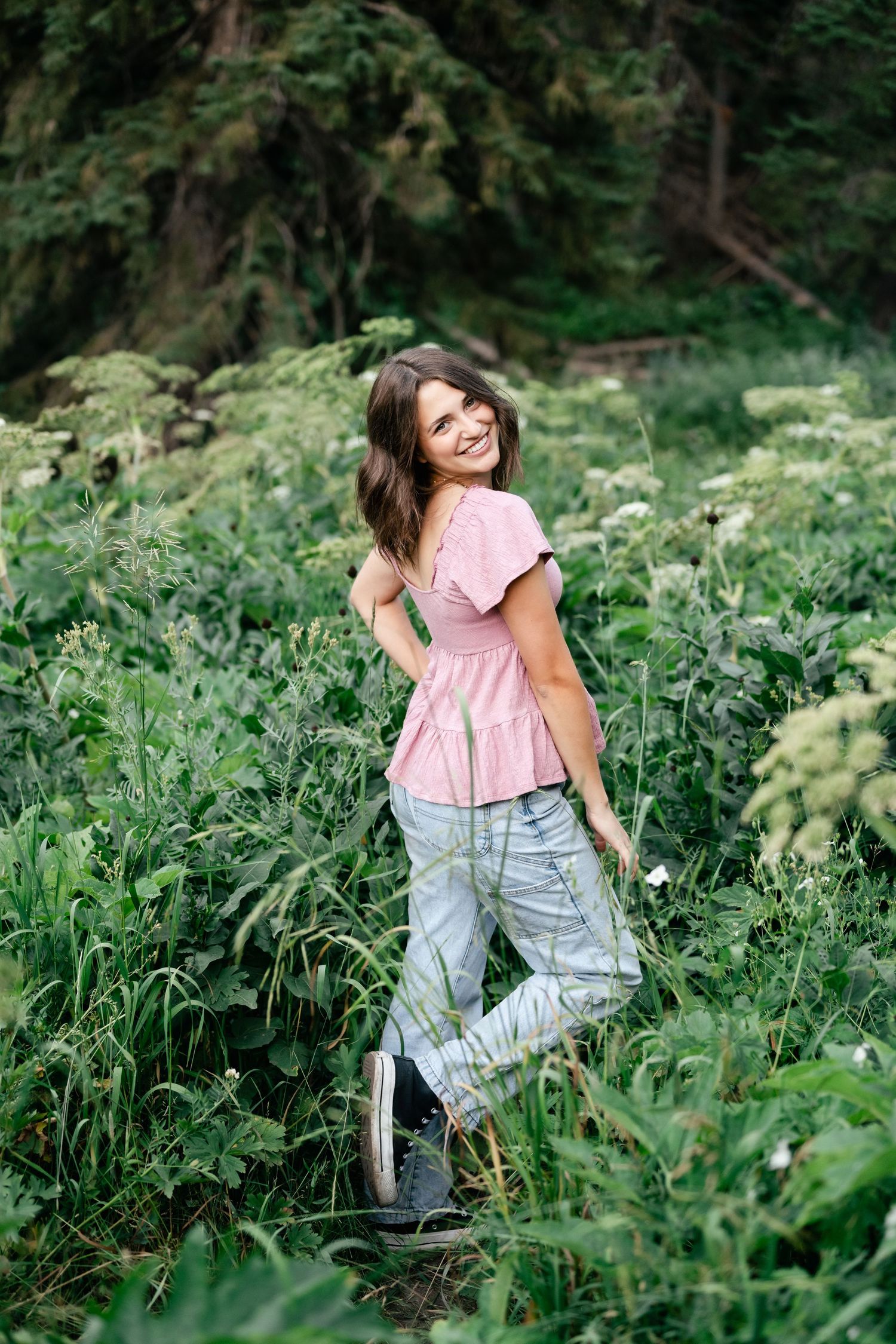 A series of outdoor portraits in lush green foliage showing playful movements in a pink top and overalls.