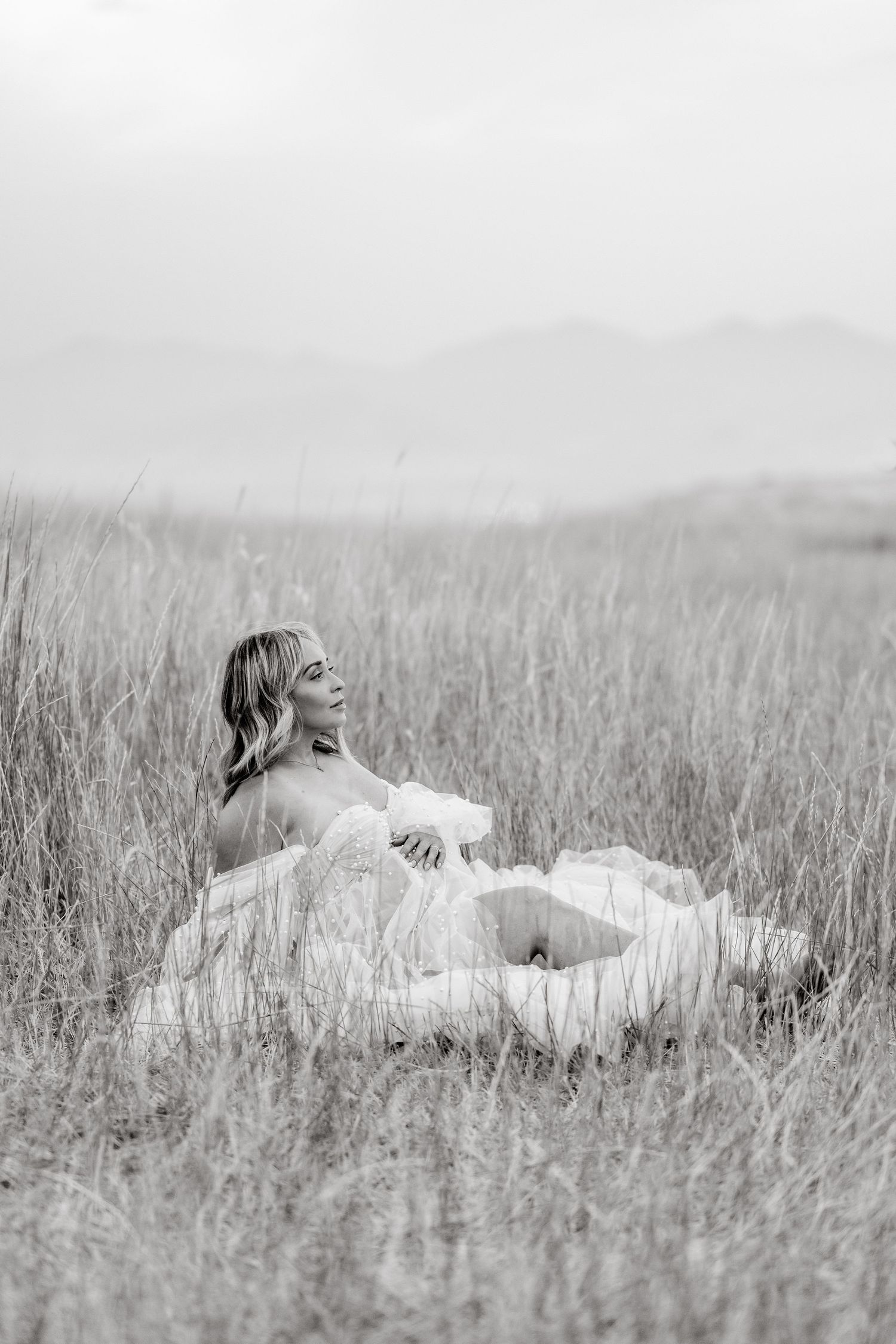 Black and white artistic photograph of a person reclining peacefully in tall grass meadow.
