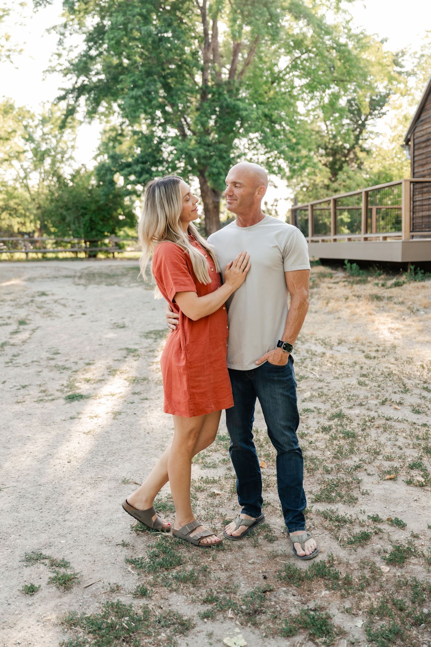 Couple in casual attire sharing tender moments together outdoors on a sunny day in a natural setting.