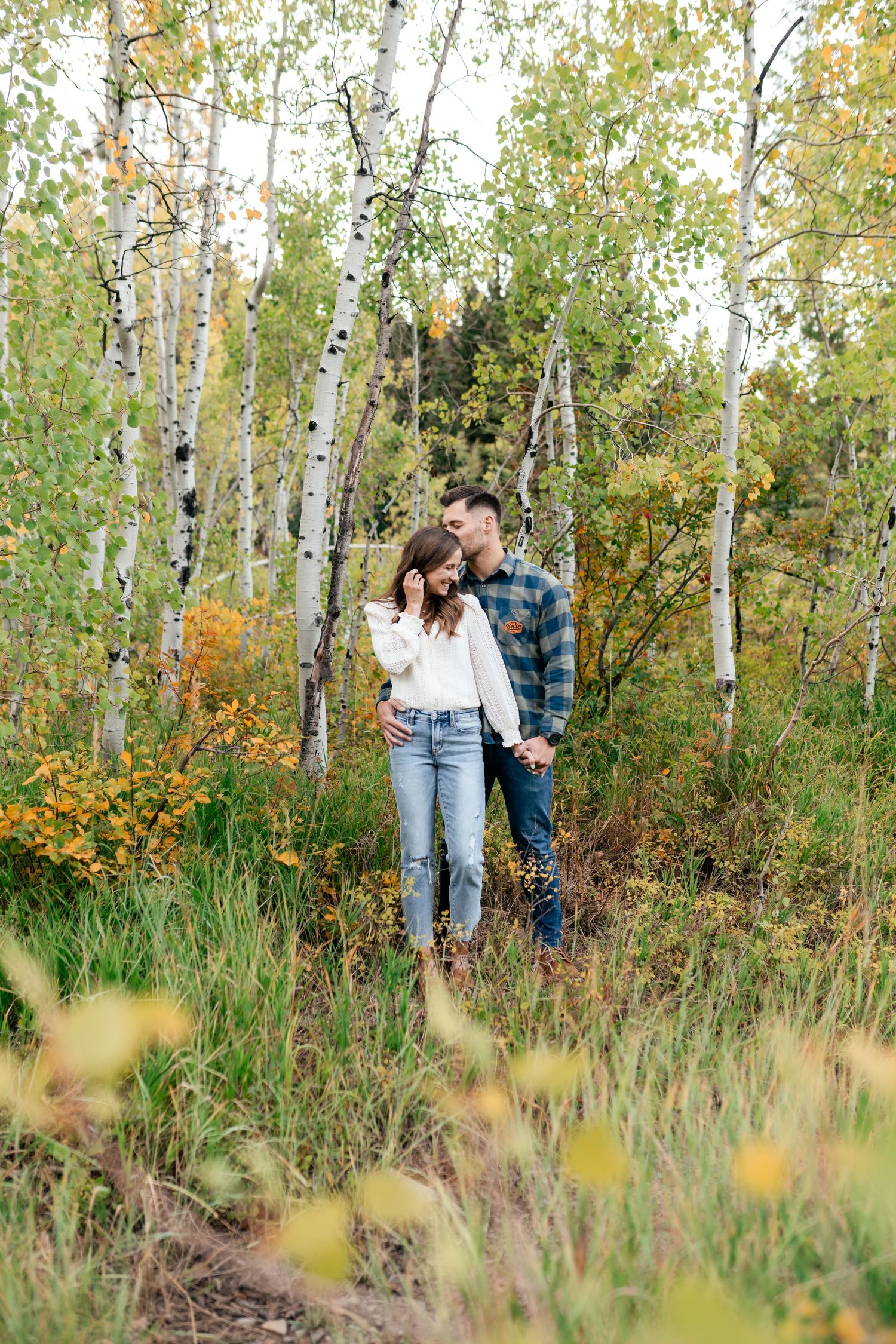 A couple stands together among white birch trees and autumn foliage.