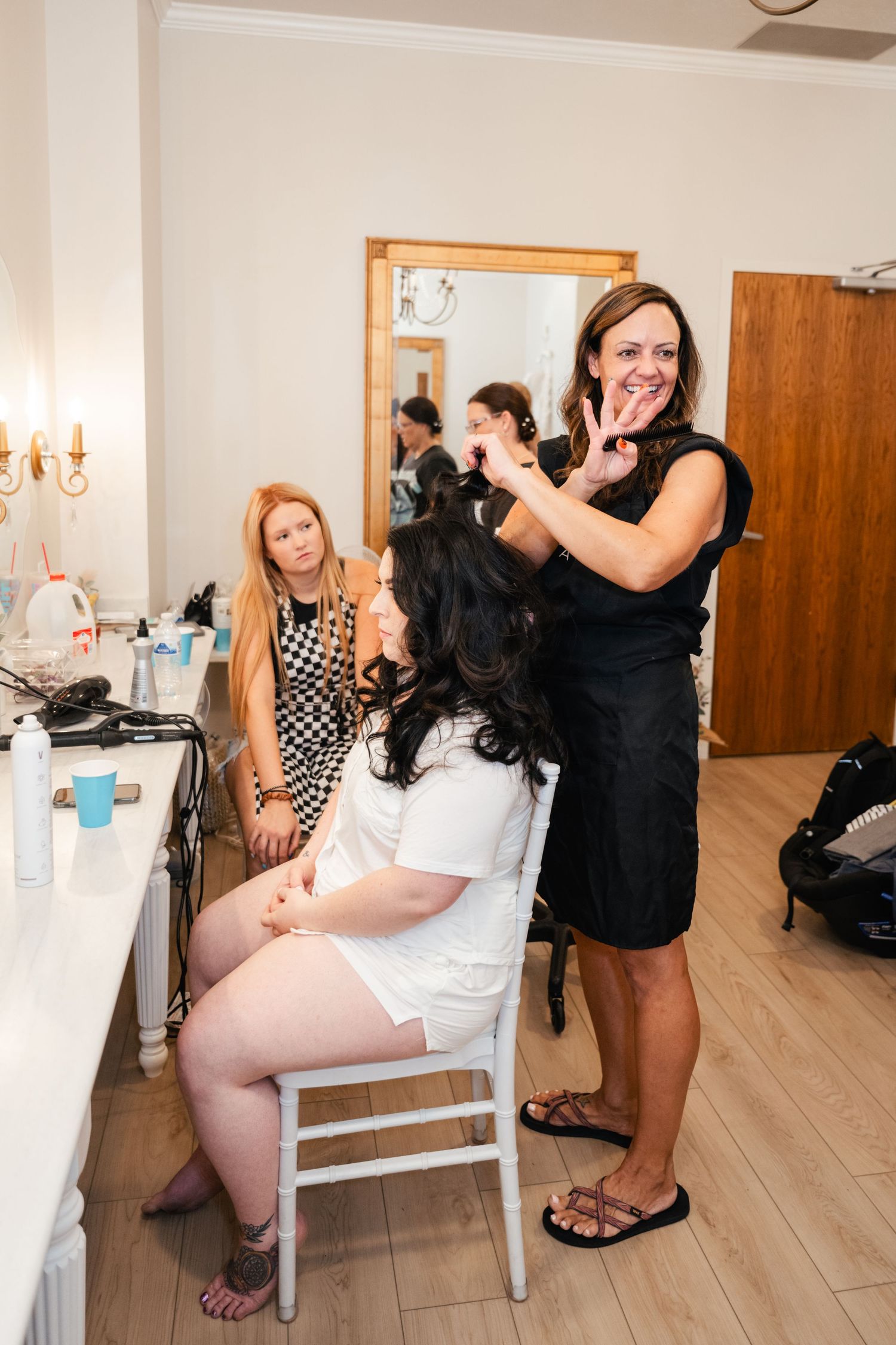 Hair and makeup preparations take place in a bright room with white walls and wooden floors.