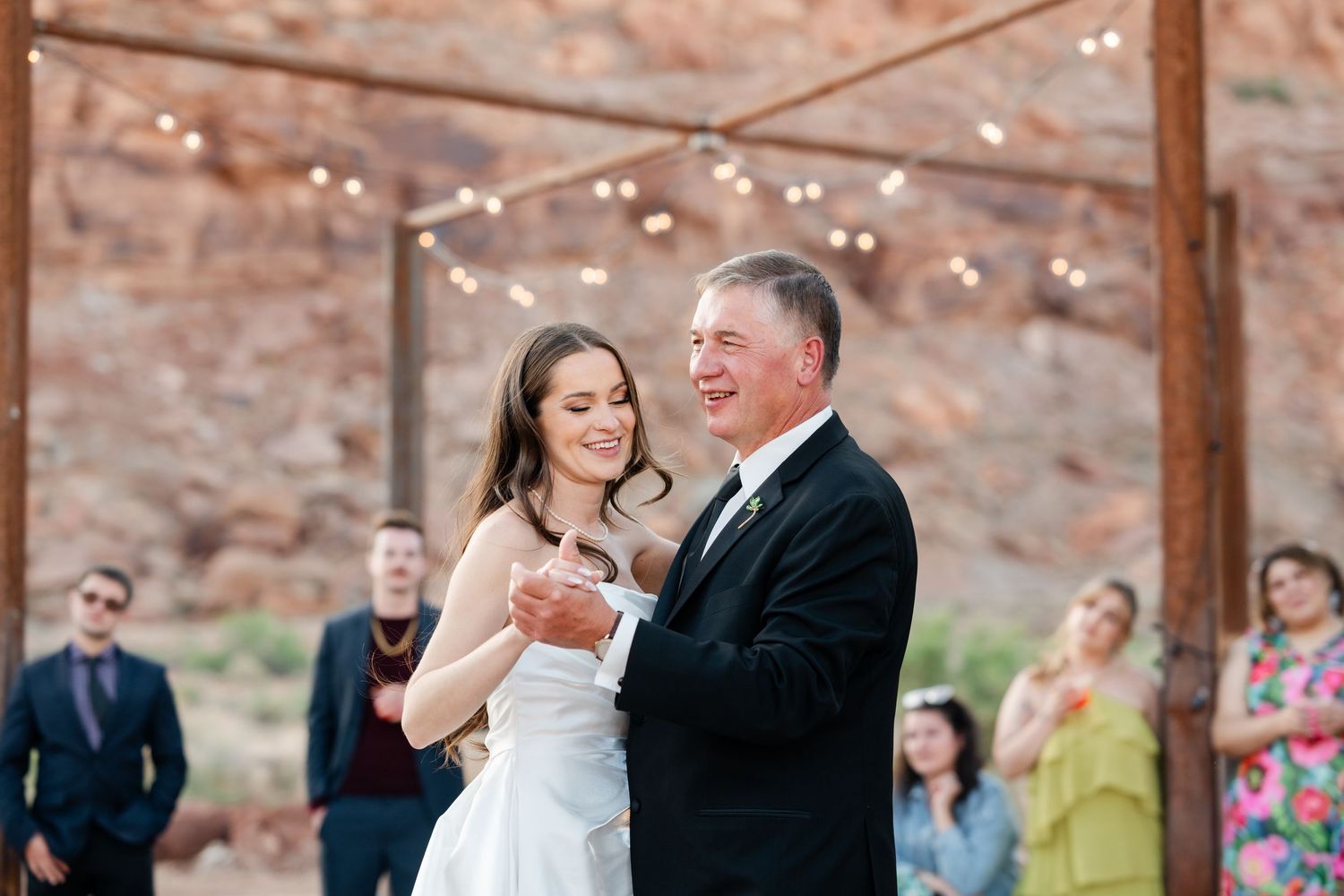 Bride and father share first dance outdoors under string lights with red rock backdrop at desert wedding reception.