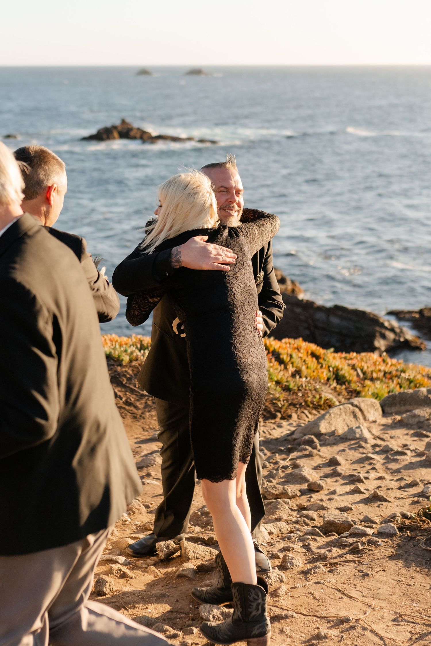 A touching moment captured during a cliffside wedding ceremony with the Pacific Ocean in the background.