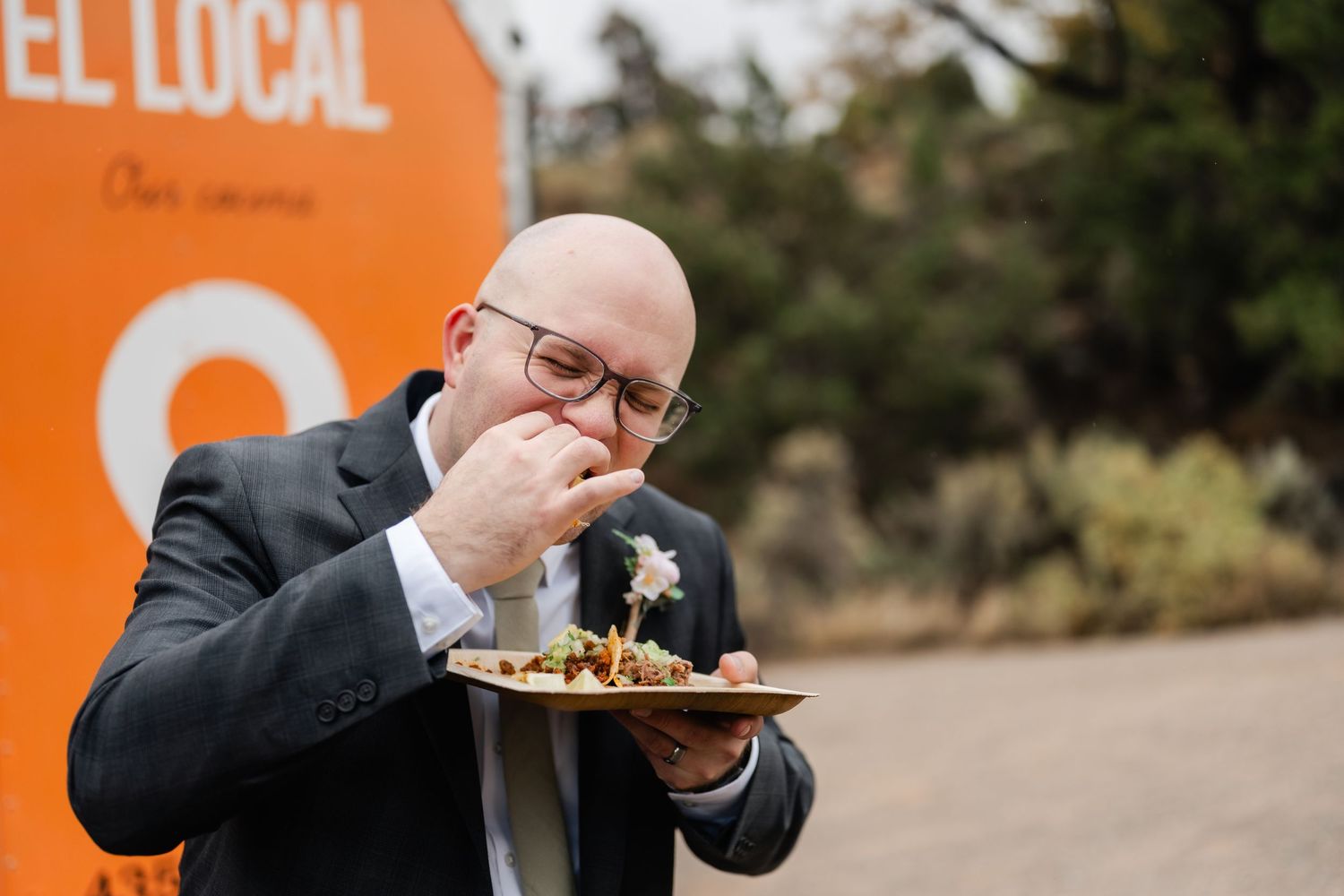 Person eating food at an event with orange backdrop and casual atmosphere.