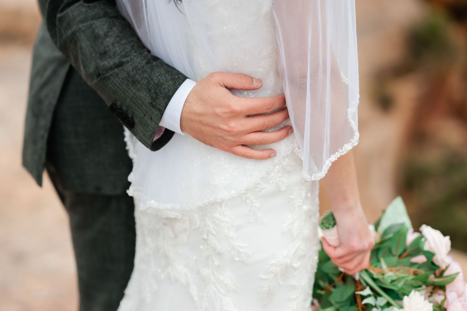 A couple in formal wedding attire holds hands while walking through a garden setting.