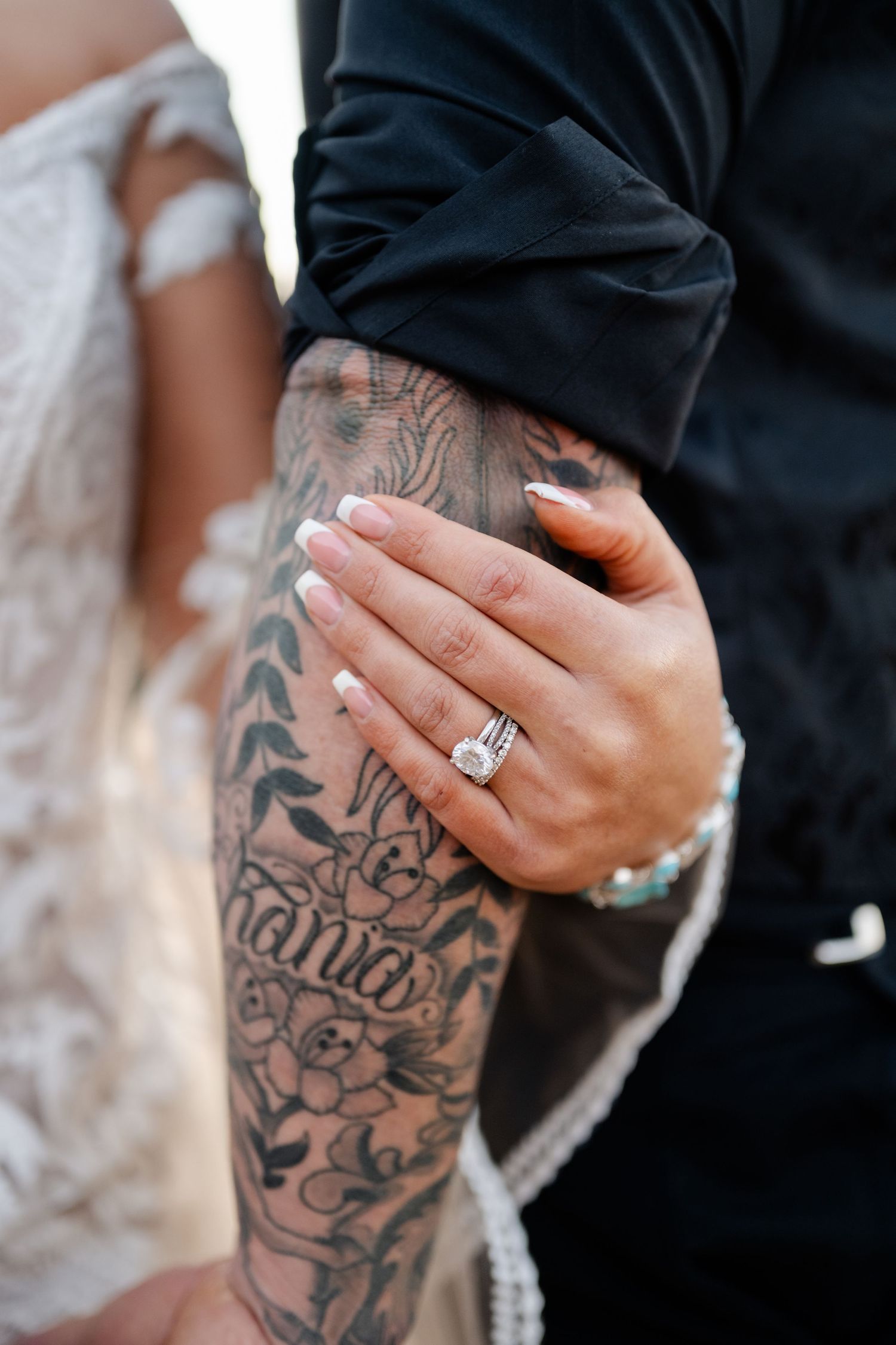 Close-up detail of hands with intricate tattoo artwork and an engagement ring.