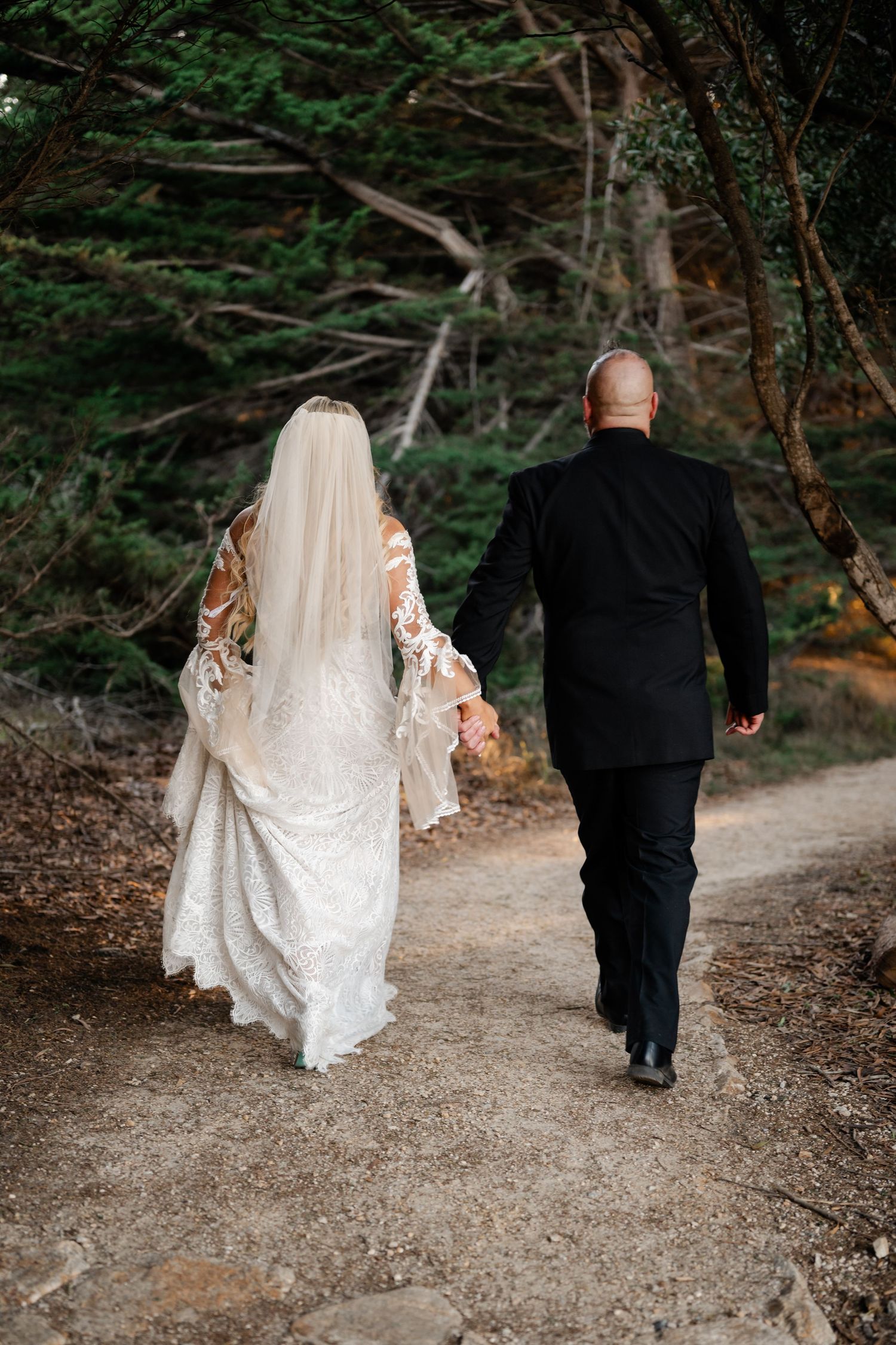 Couple walking along wooded forest path in formal attire.