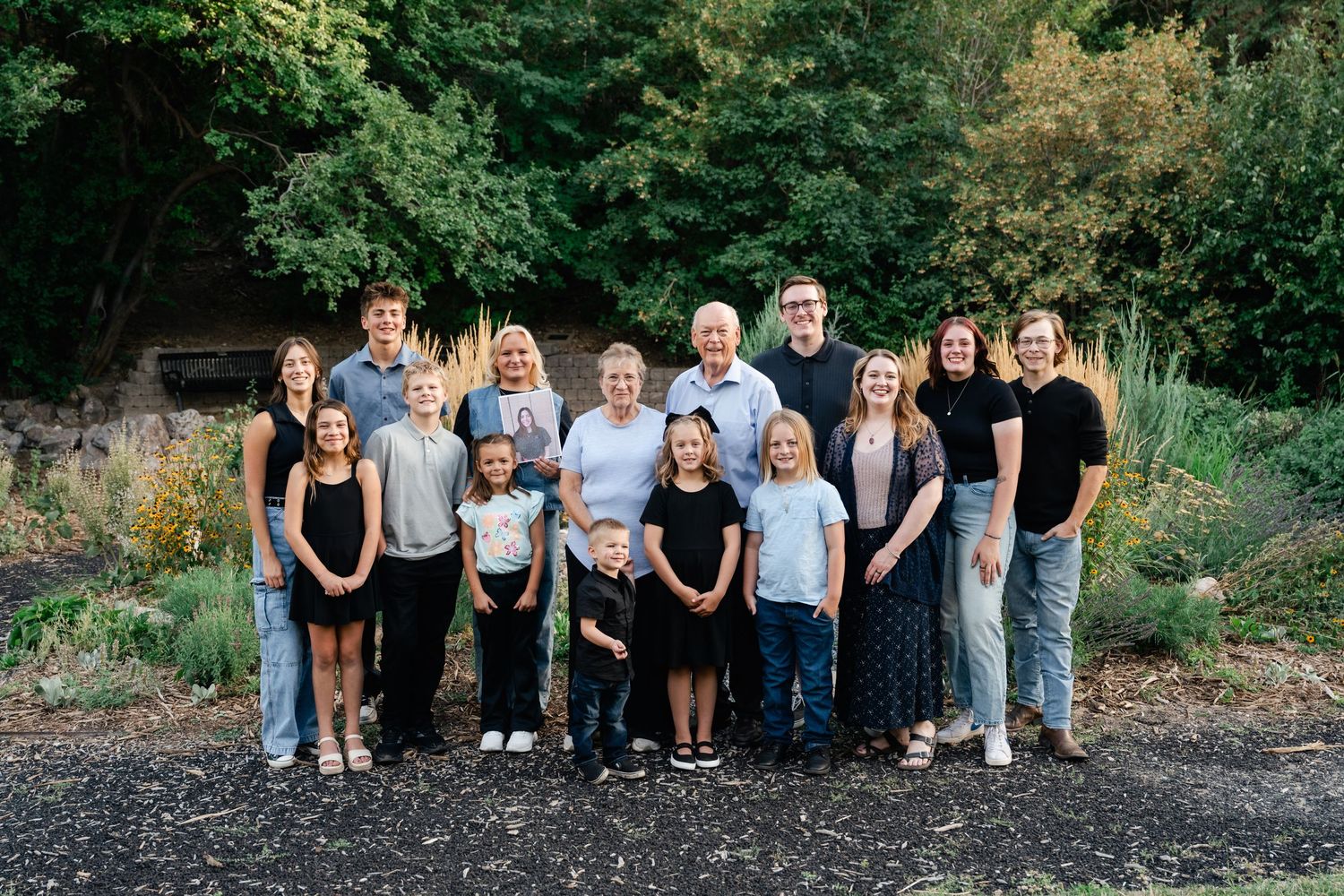 A group of people wearing casual clothing pose together outdoors against a natural backdrop of trees and foliage.