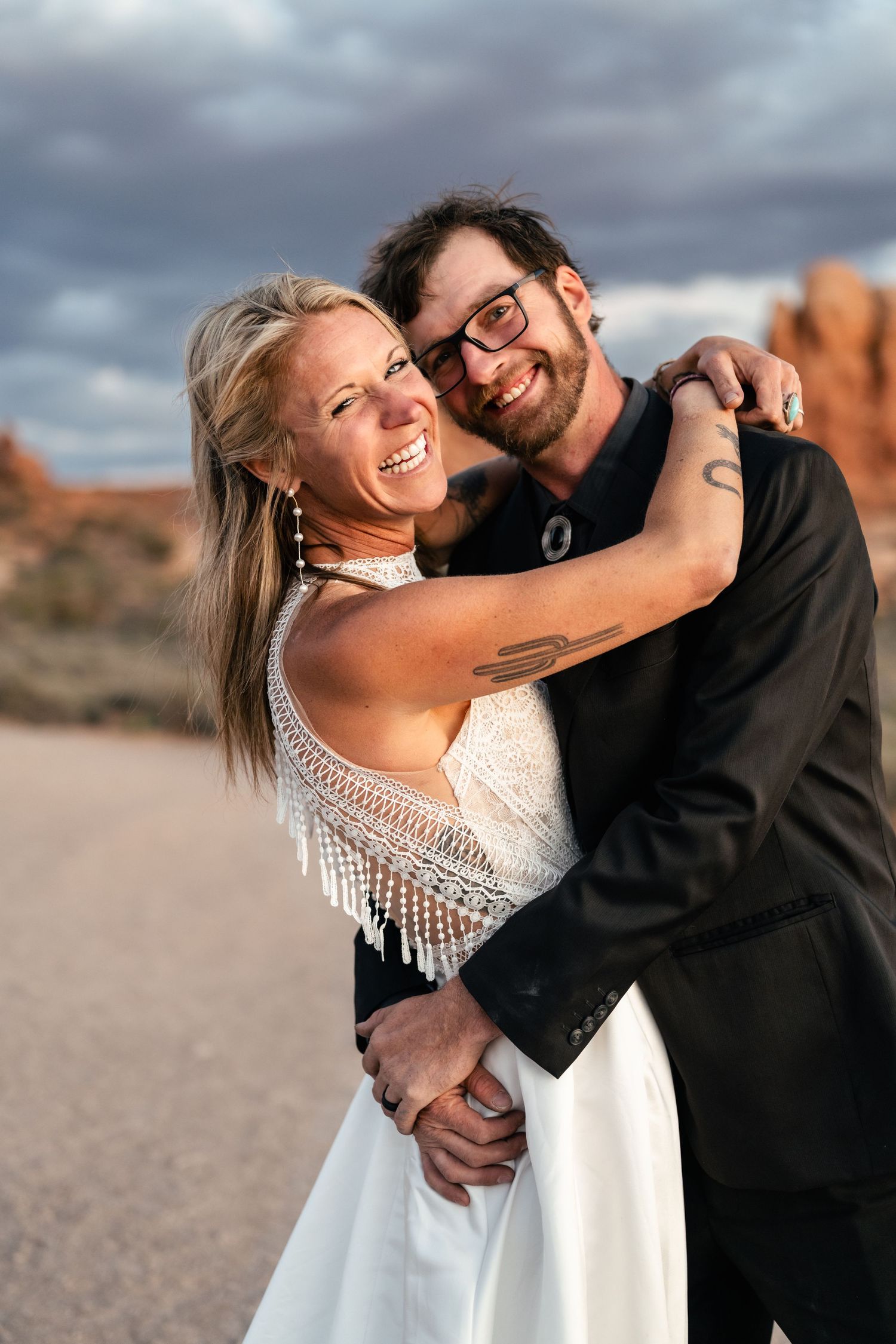 A happy couple embraces and laughs together during a desert photo session with dramatic cloudy skies.