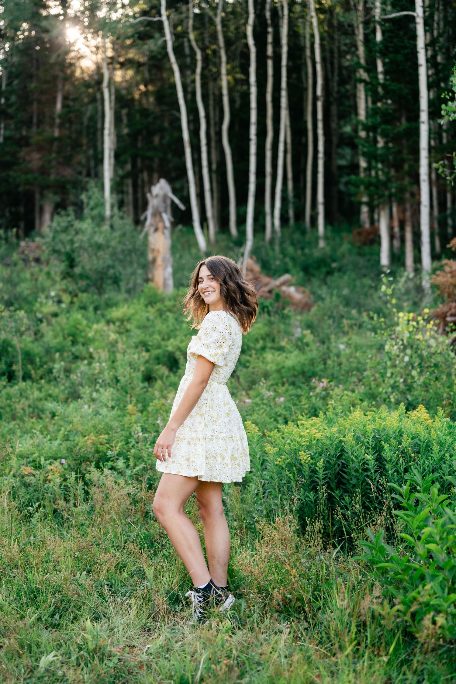 A person in a white dress twirls playfully in a lush forest setting at sunset.