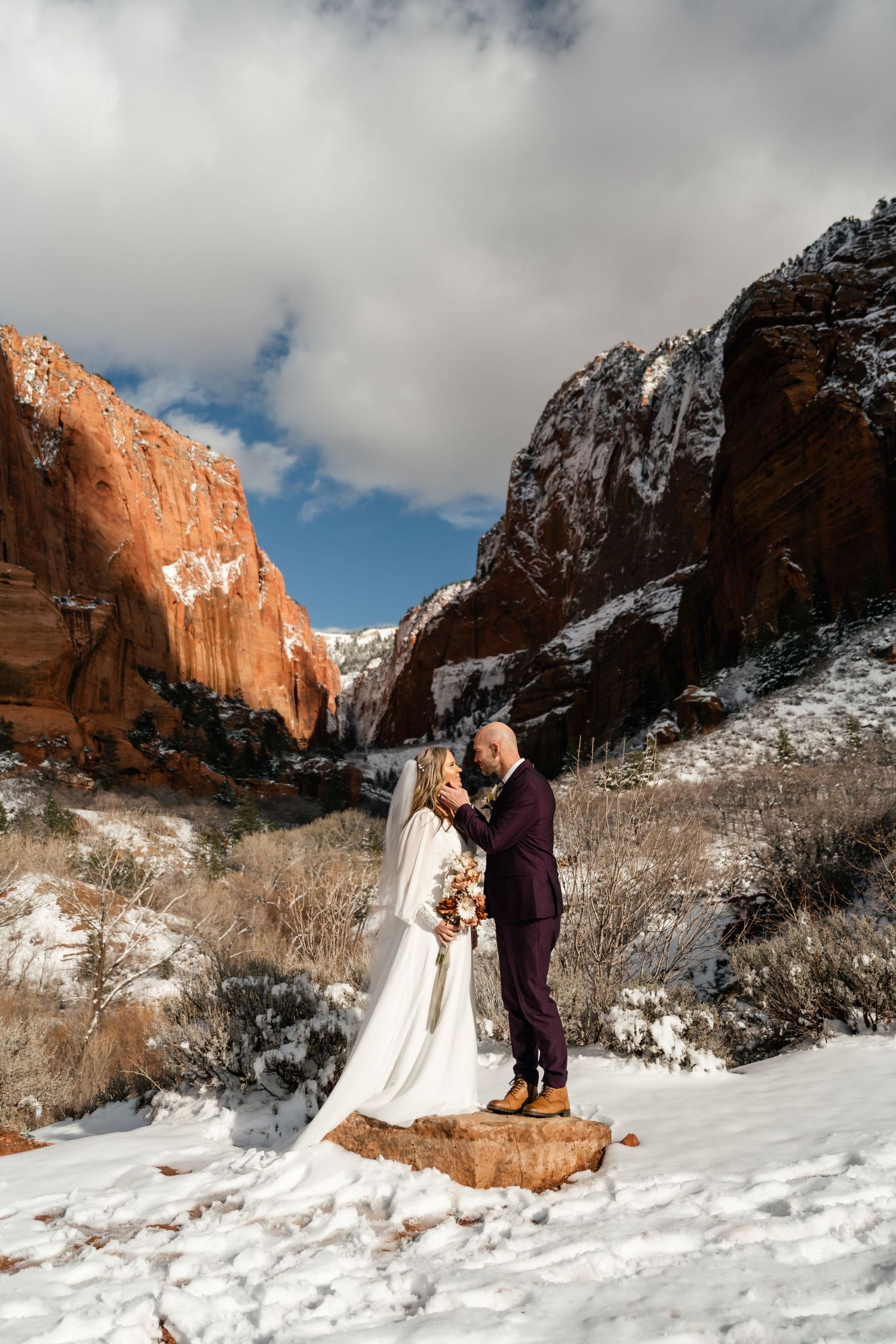 Winter wedding scene with snow-covered ground and towering red canyon walls in the background.