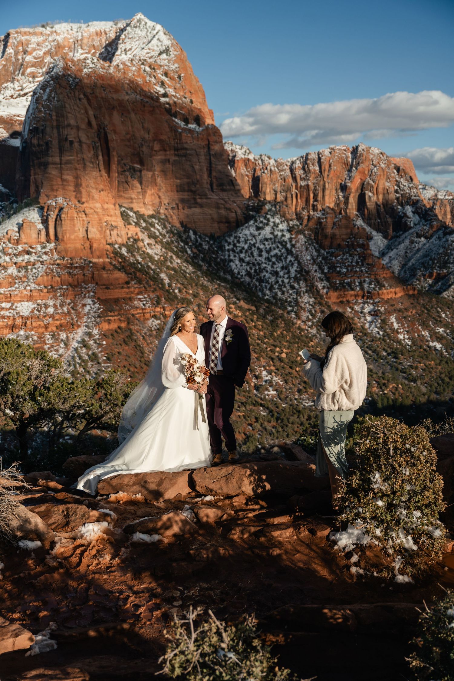 Intimate wedding ceremony on red rocks overlooking a majestic snow-dusted canyon landscape.