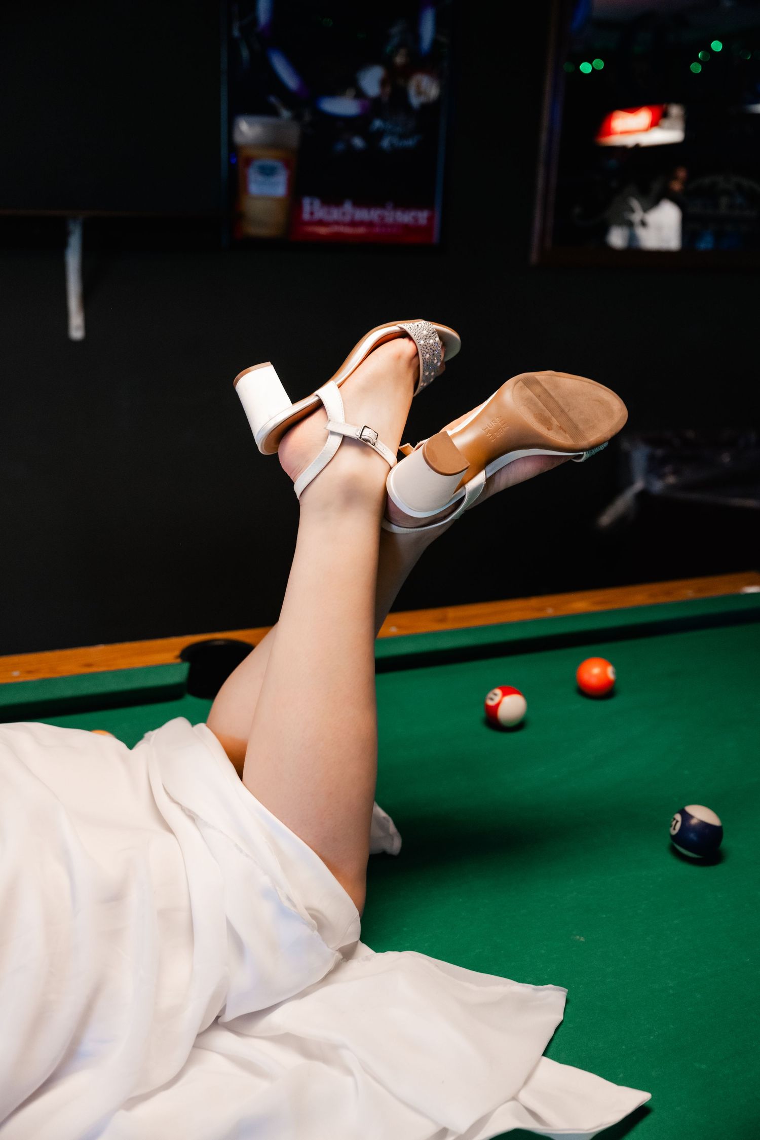 White high heel shoe rests on a green pool table with billiard balls in the background.