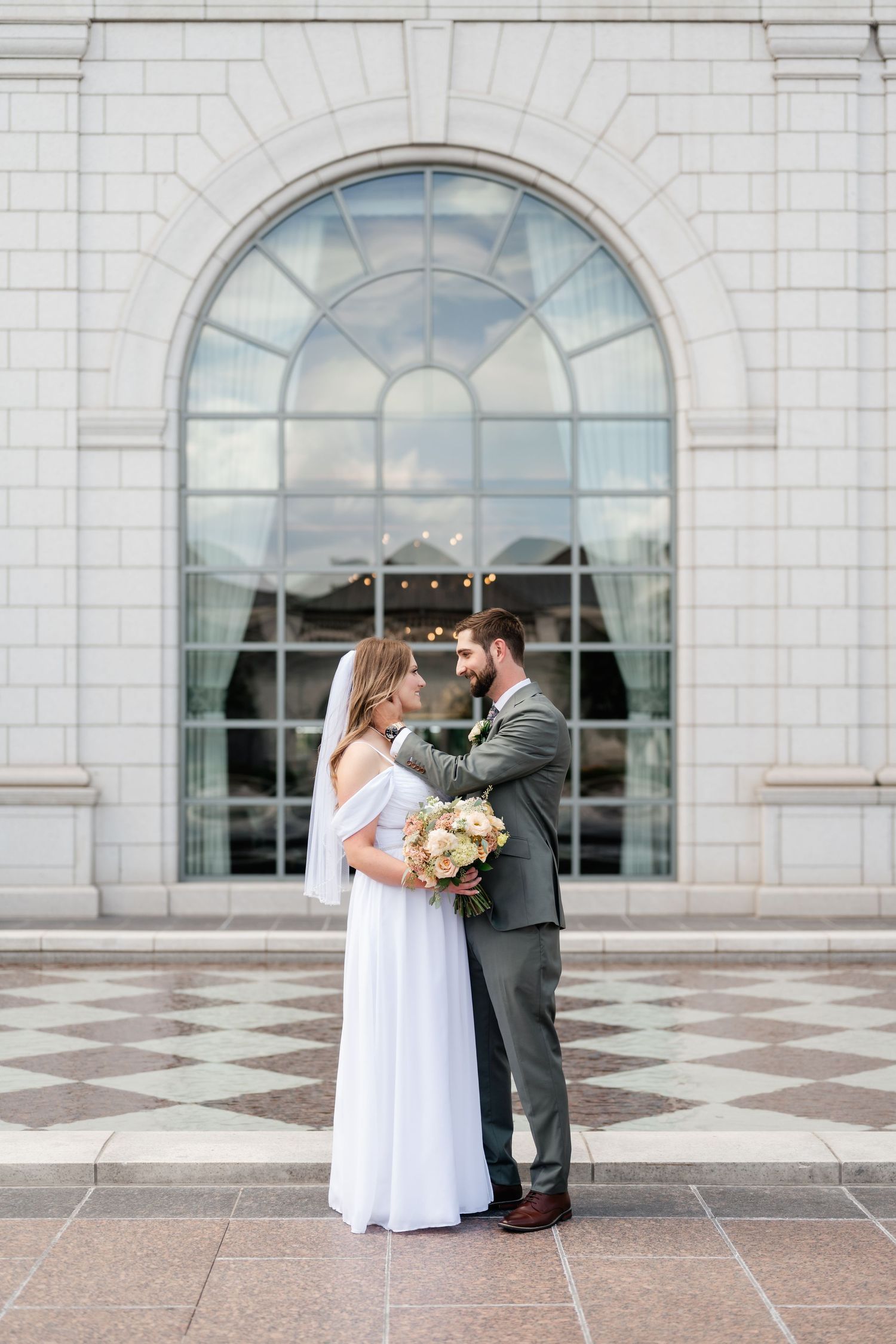 A couple shares an intimate moment on a grand stone terrace with arched windows in the background.