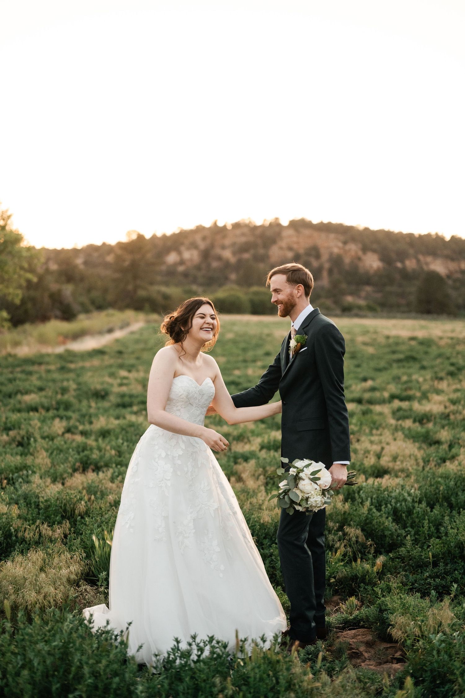 Newlyweds share playful moment while dancing in natural outdoor setting.