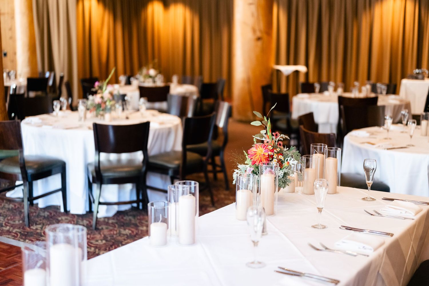 Elegant wedding reception venue with round tables, white linens, and delicate floral centerpieces in glass vases.
